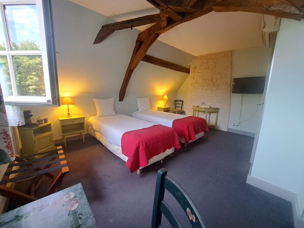 A bedroom with a large bed, two bedside tables with lamps, a small table with a chair, and a TV on the wall.