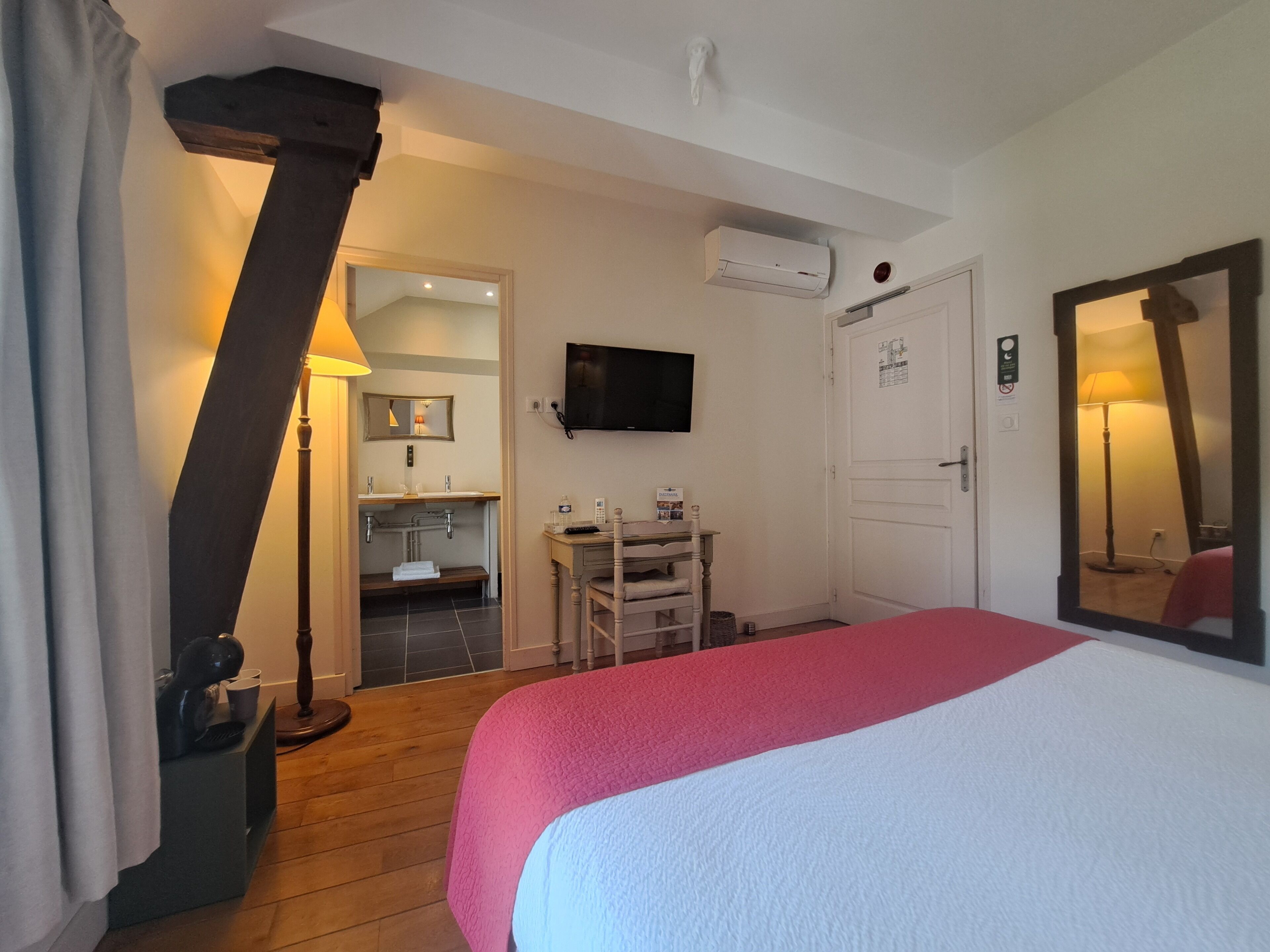 A hotel room with a bed, a desk, a chair, a television, and an air conditioning unit.