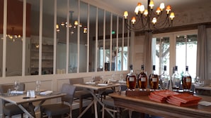 Ein Restaurant mit hohen Decken, großen Fenstern und einer Kristallleuchter. Die Tische sind mit Weingläsern und Flaschen gedeckt.