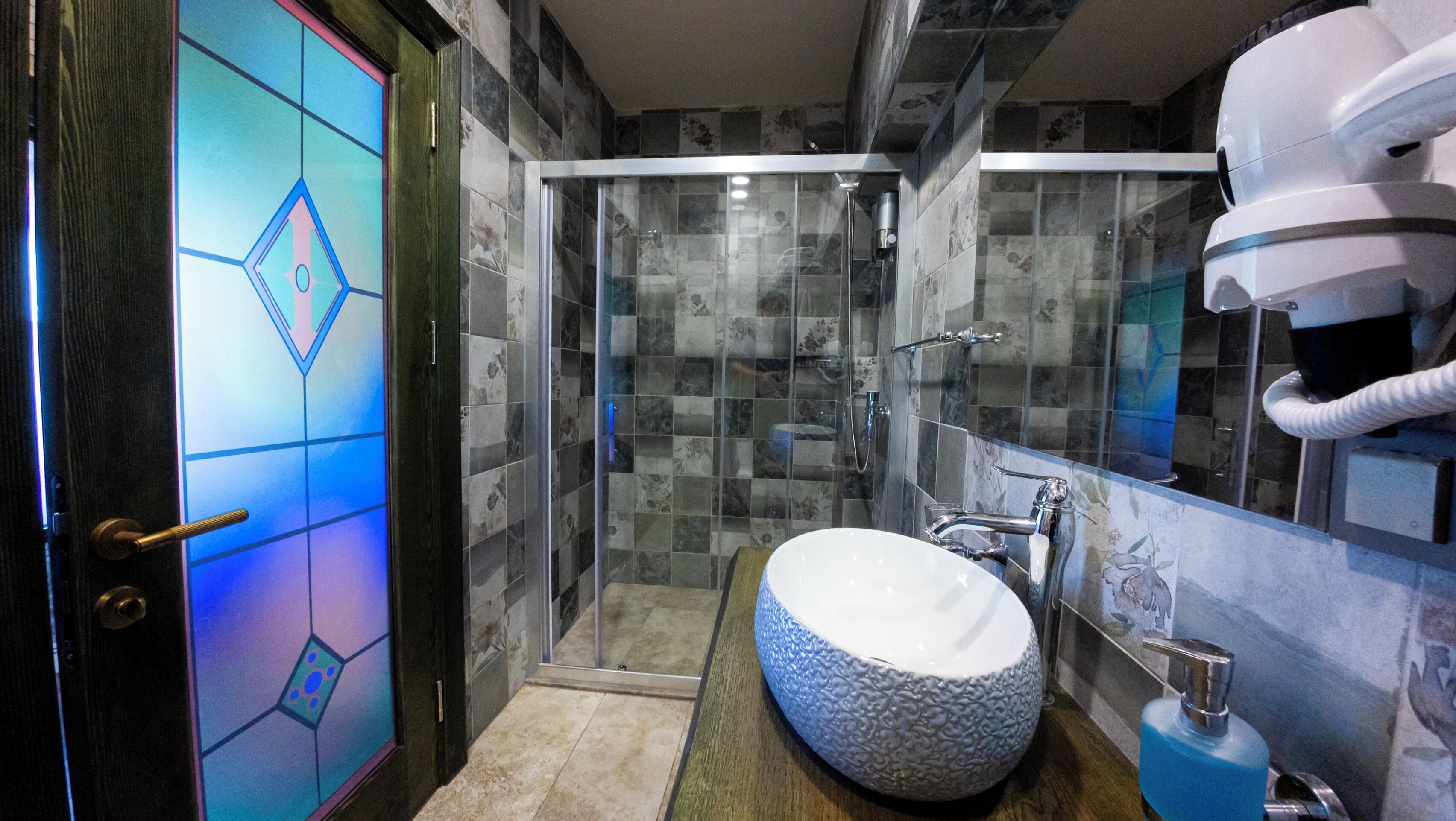 A modern bathroom with a glass-enclosed shower, a large decorative sink, and a mirror with a towel rack.