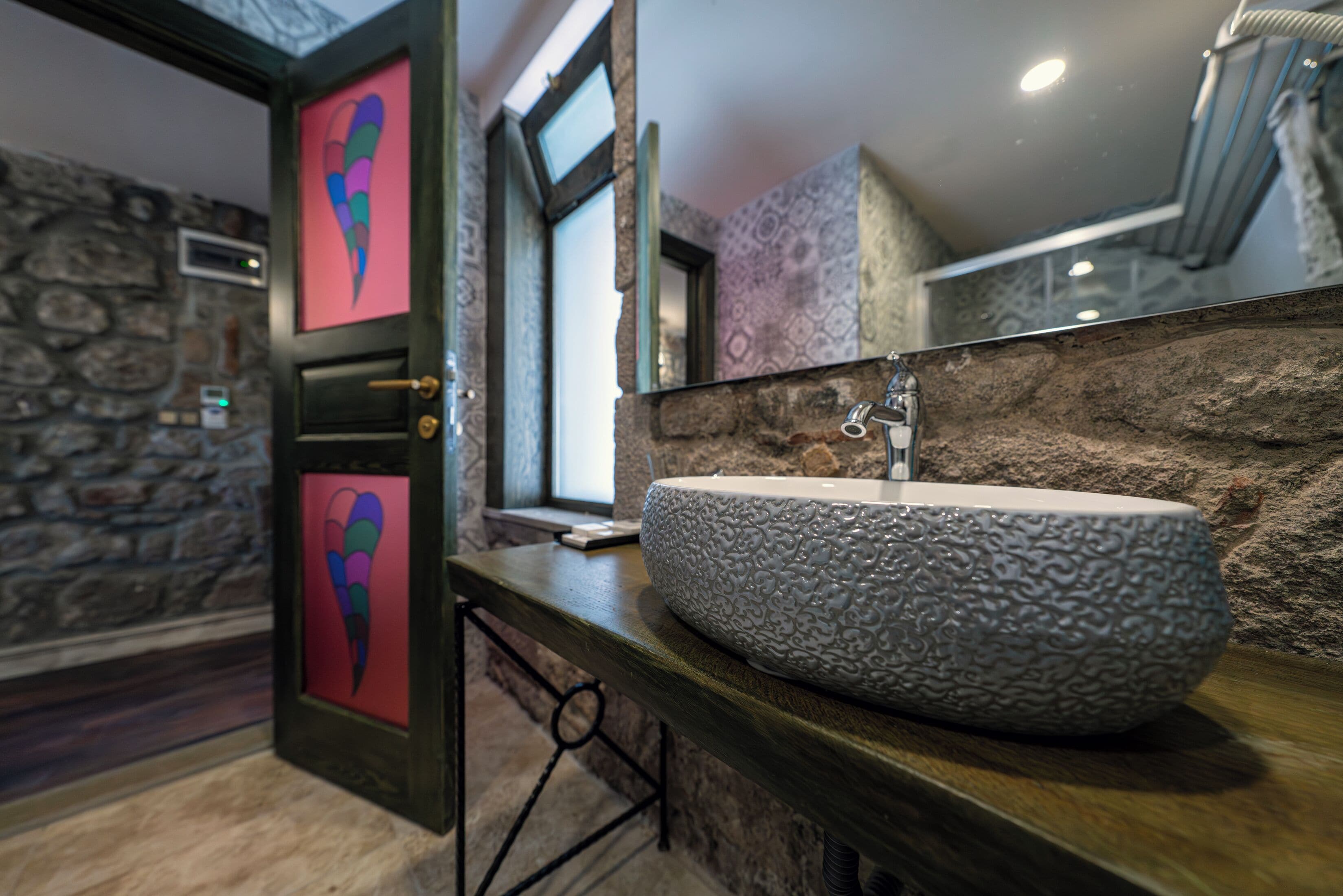 A bathroom with a stone wall, a large sink, and a window.