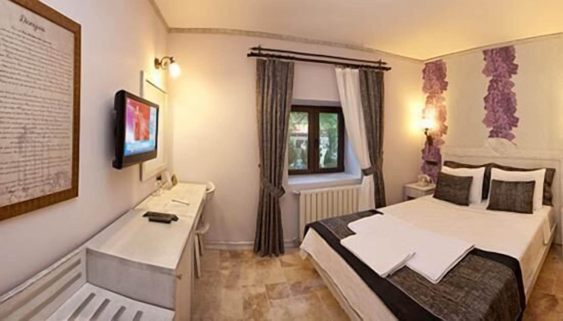 Ein Hotelzimmer mit einem Bett, einem Schreibtisch, einem Fernseher und einem Fenster mit Vorhängen.