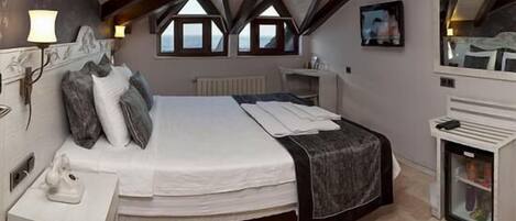 A bedroom with a large bed, a bedside table, a dresser, a mirror, and a window with a view.