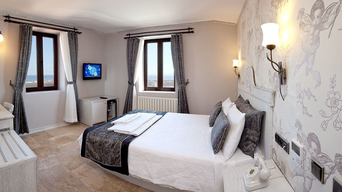 Ein Schlafzimmer mit Bett, Nachttisch, Lampe und Meerblick aus dem Fenster.