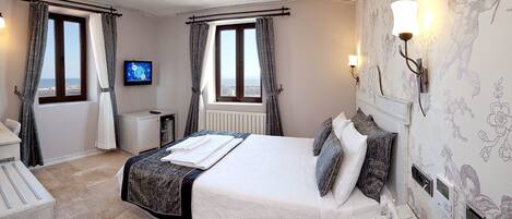 A bedroom with a bed, bedside table, lamp, and a view of the sea through the window.
