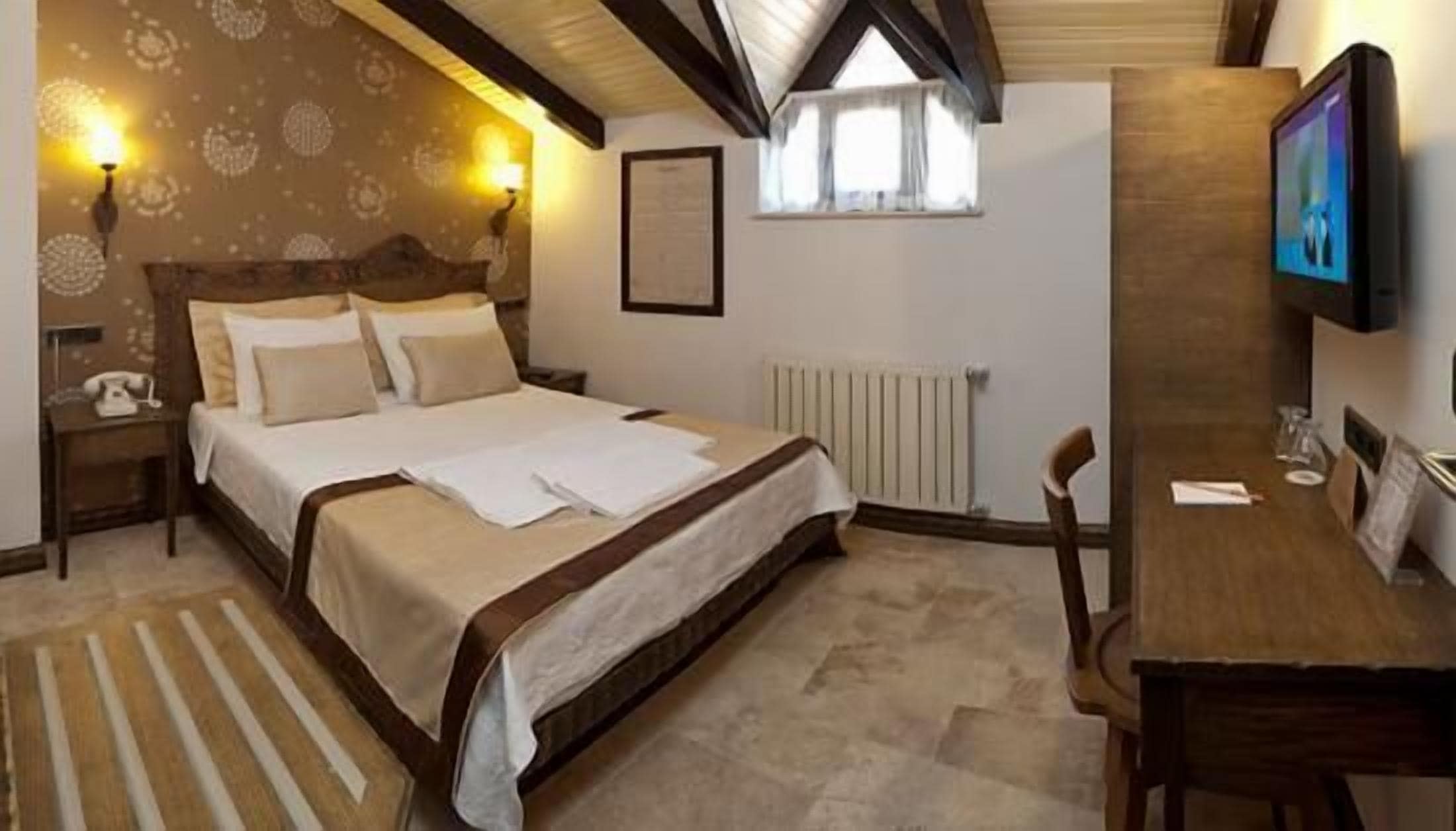 A bedroom with a bed, bedside tables, a desk, a chair, a television, and a window.