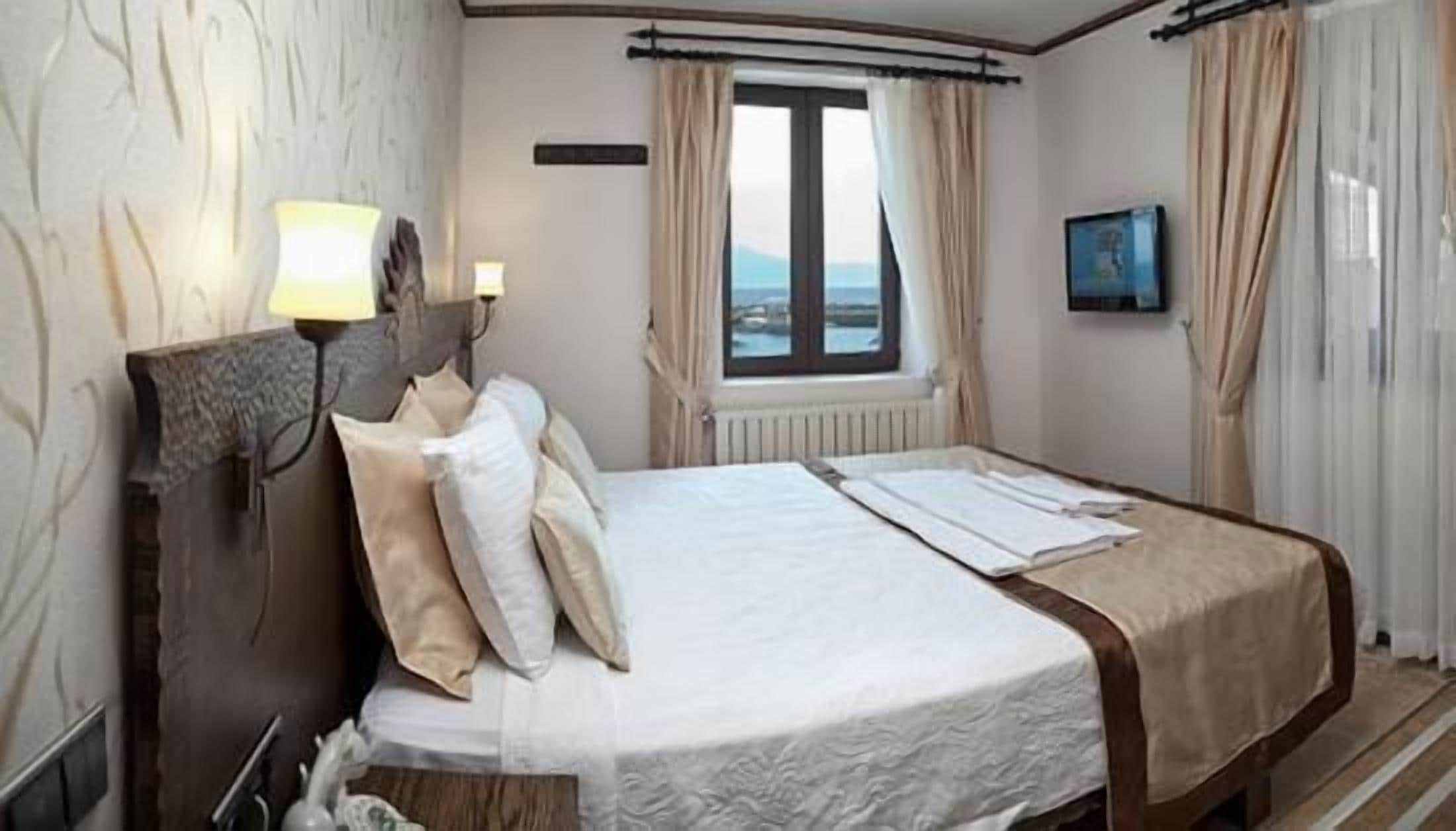 A hotel room with a bed, a nightstand, a window with curtains, and a view of the sea.