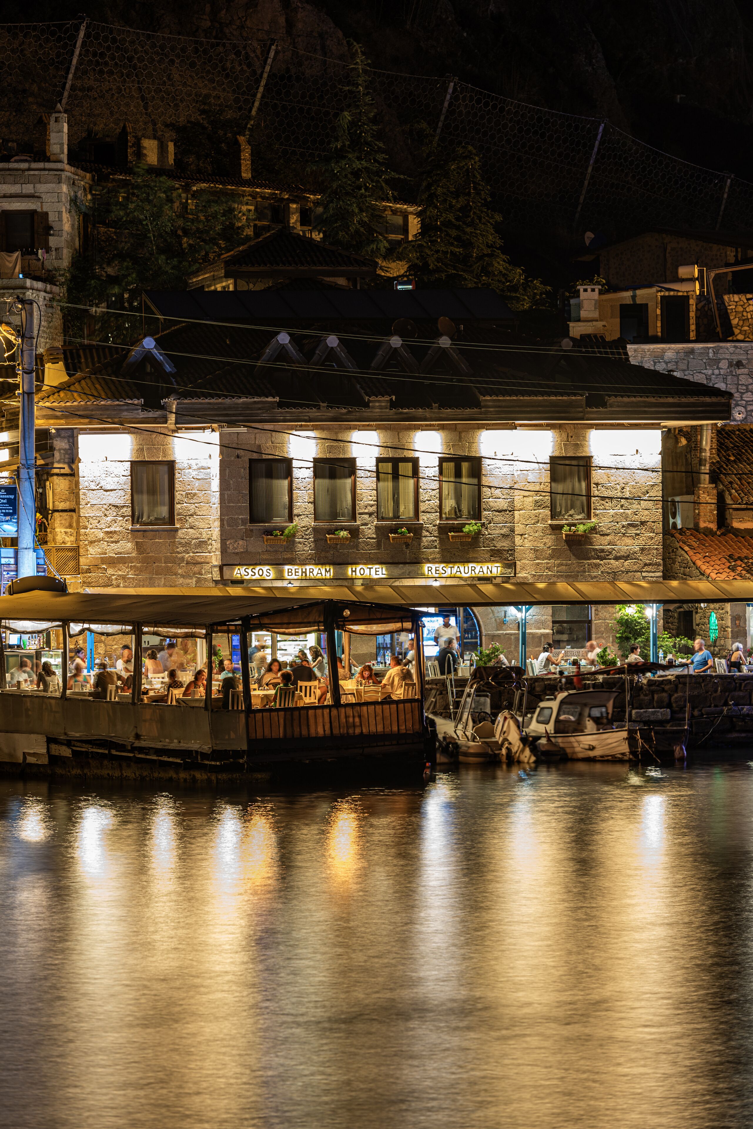 A stone building with a sign reading "Assos Behram Hotel Restaurant" at night.