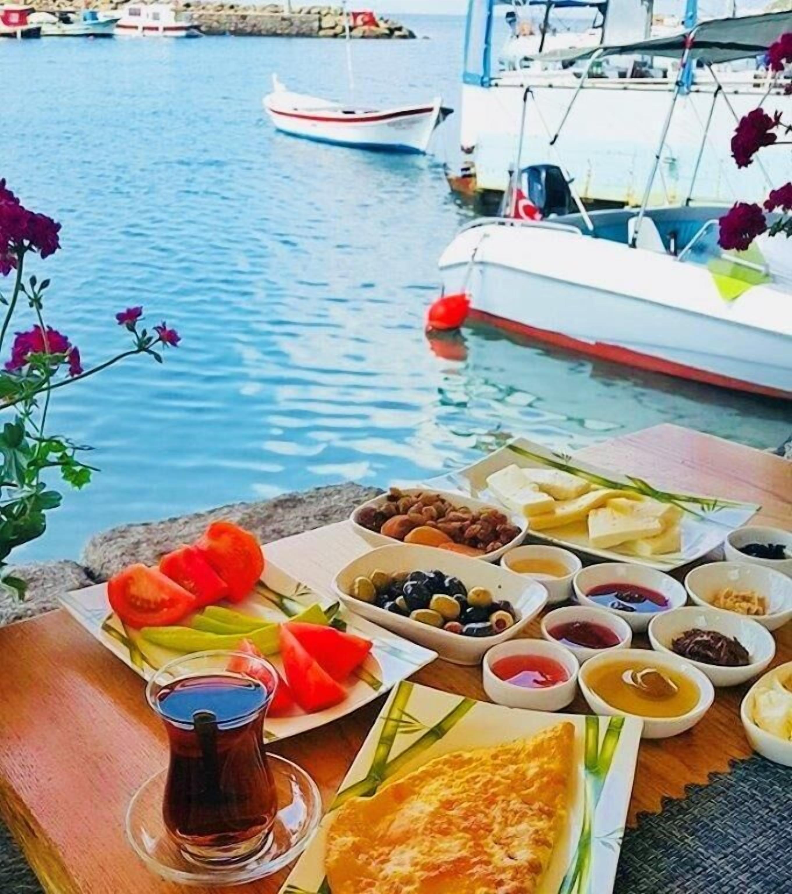 Una mesa con distintos alimentos y un vaso de té, con un fondo de barcos en el agua.