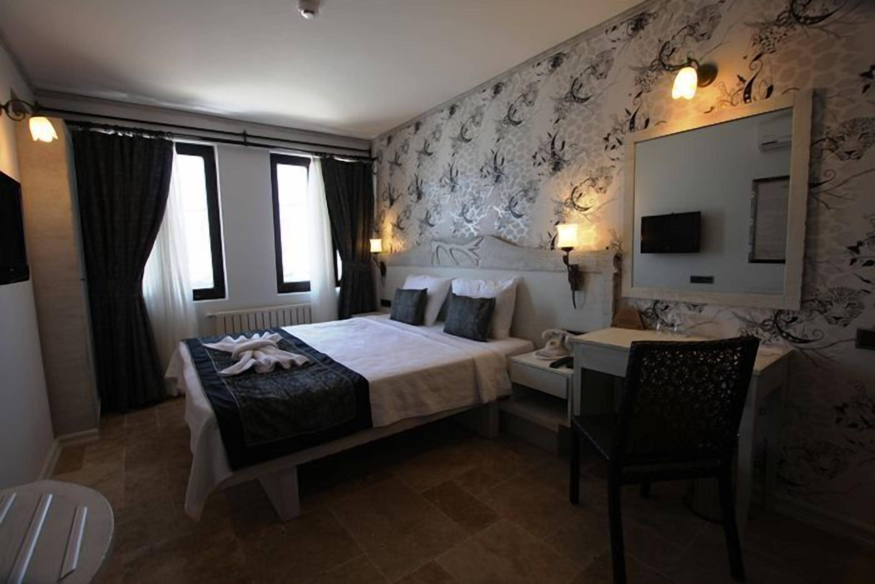 Habitación de hotel con cama, mesita de noche, silla y un espejo grande.