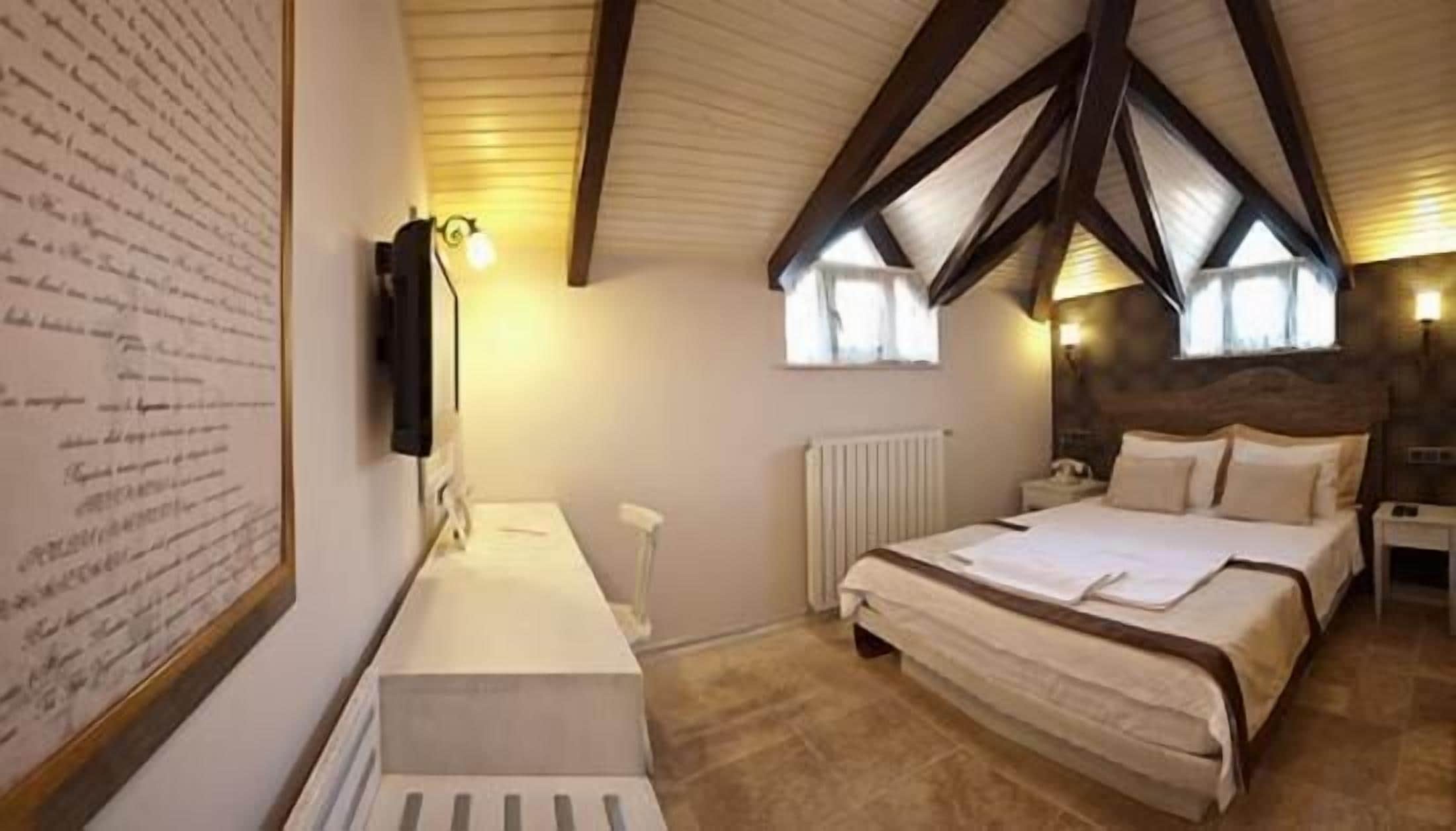 A bedroom with a large bed, a bedside table, a wall-mounted TV, and a window with curtains.