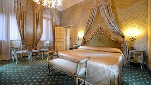 Une chambre d’hôtel classique, dotée d’un grand lit, de rideaux décoratifs, d’un lustre et d’une moquette à motifs verts.