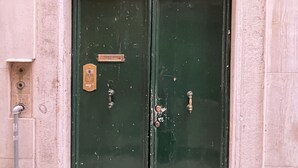 A green double door with a metal grid above it, a small plaque, and a metal handle. - Ca' Rialto House (Venice)