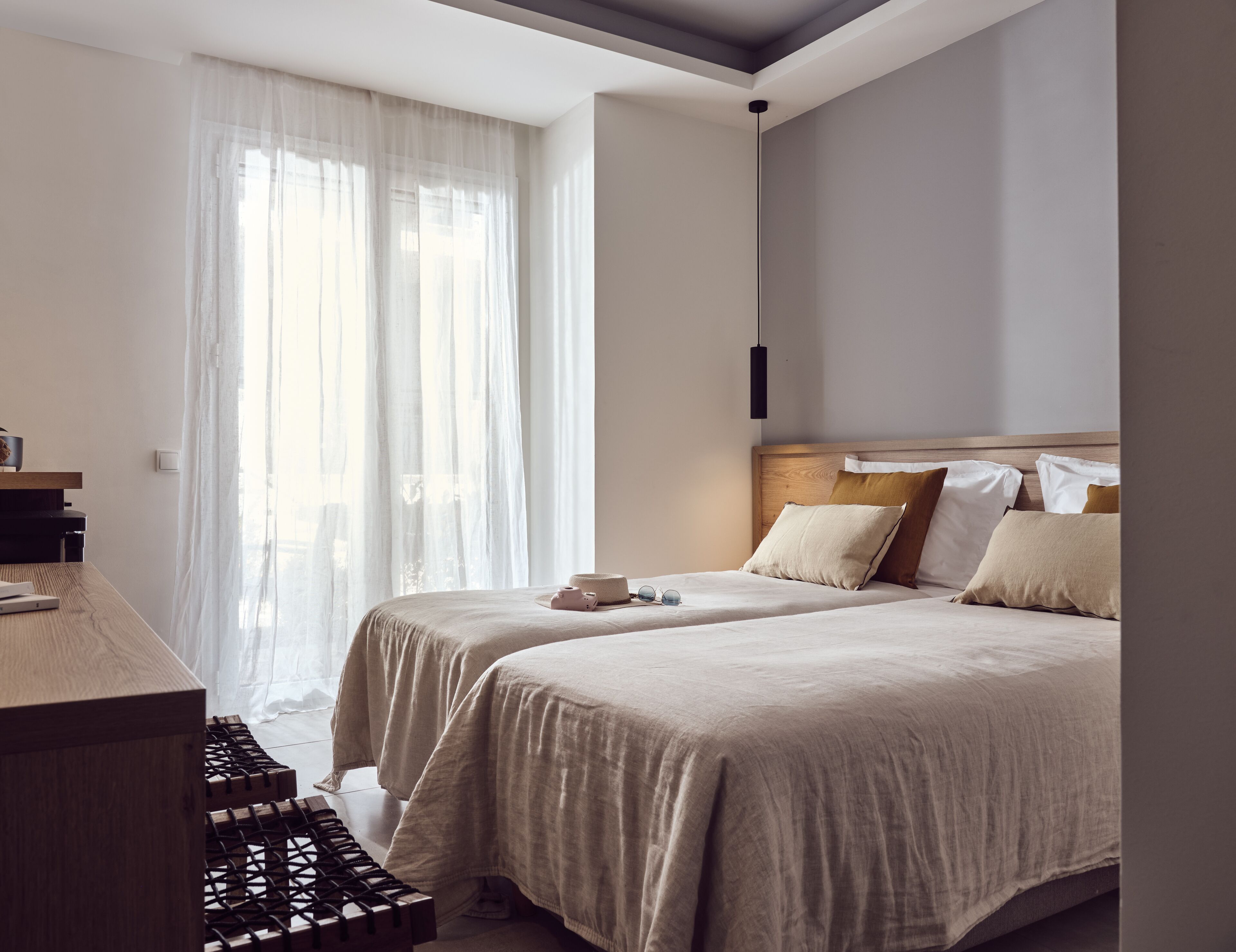 A bedroom with two beds, a desk, and a large window with sheer curtains.
