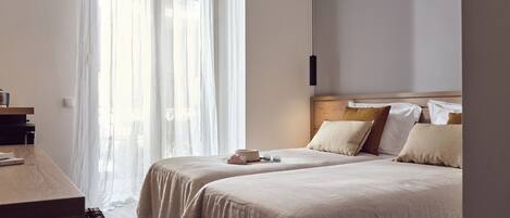 A bedroom with two beds, a desk, and a large window with sheer curtains.