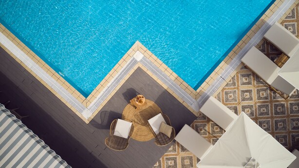 An aerial view of a swimming pool with a tiled deck, two wicker chairs with cushions, and a patterned floor. - Cactus Hotel (Zakynthos)