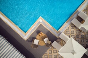 An aerial view of a swimming pool with a tiled deck, two wicker chairs with cushions, and a patterned floor.