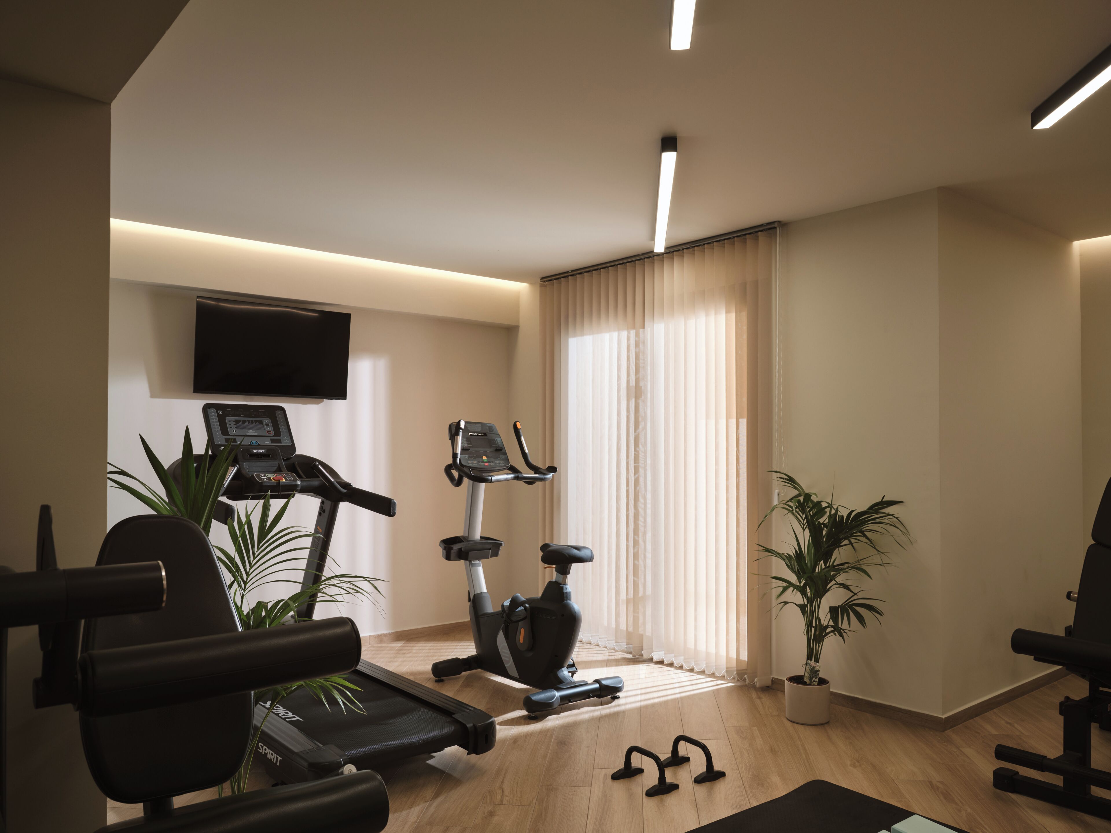 Une salle de sport à domicile équipée de matériel d’exercice, d’un téléviseur et d’une grande fenêtre avec des rideaux.