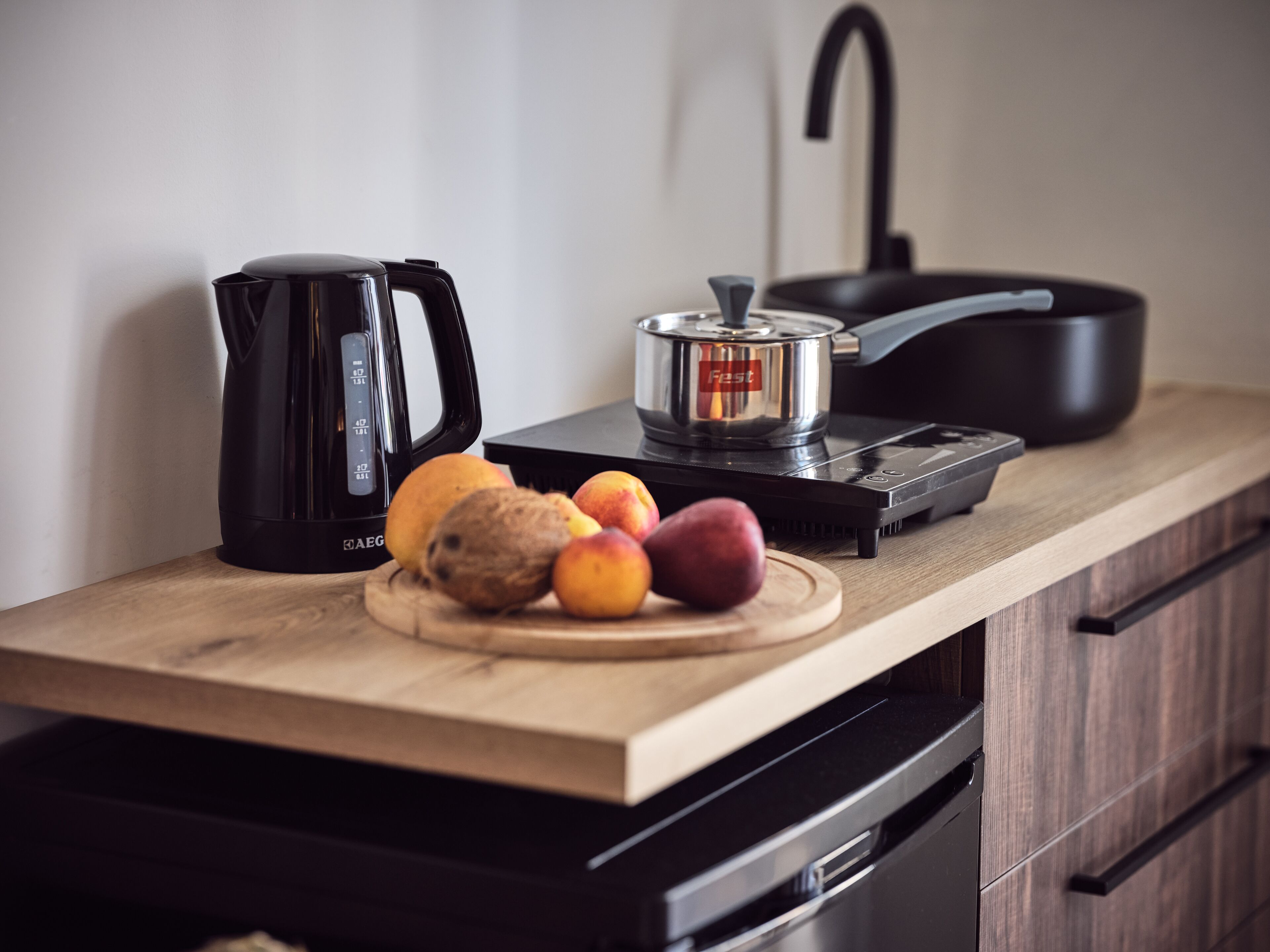 A kitchen counter with a coffee maker, a slow cooker, and a cutting board with fruits.