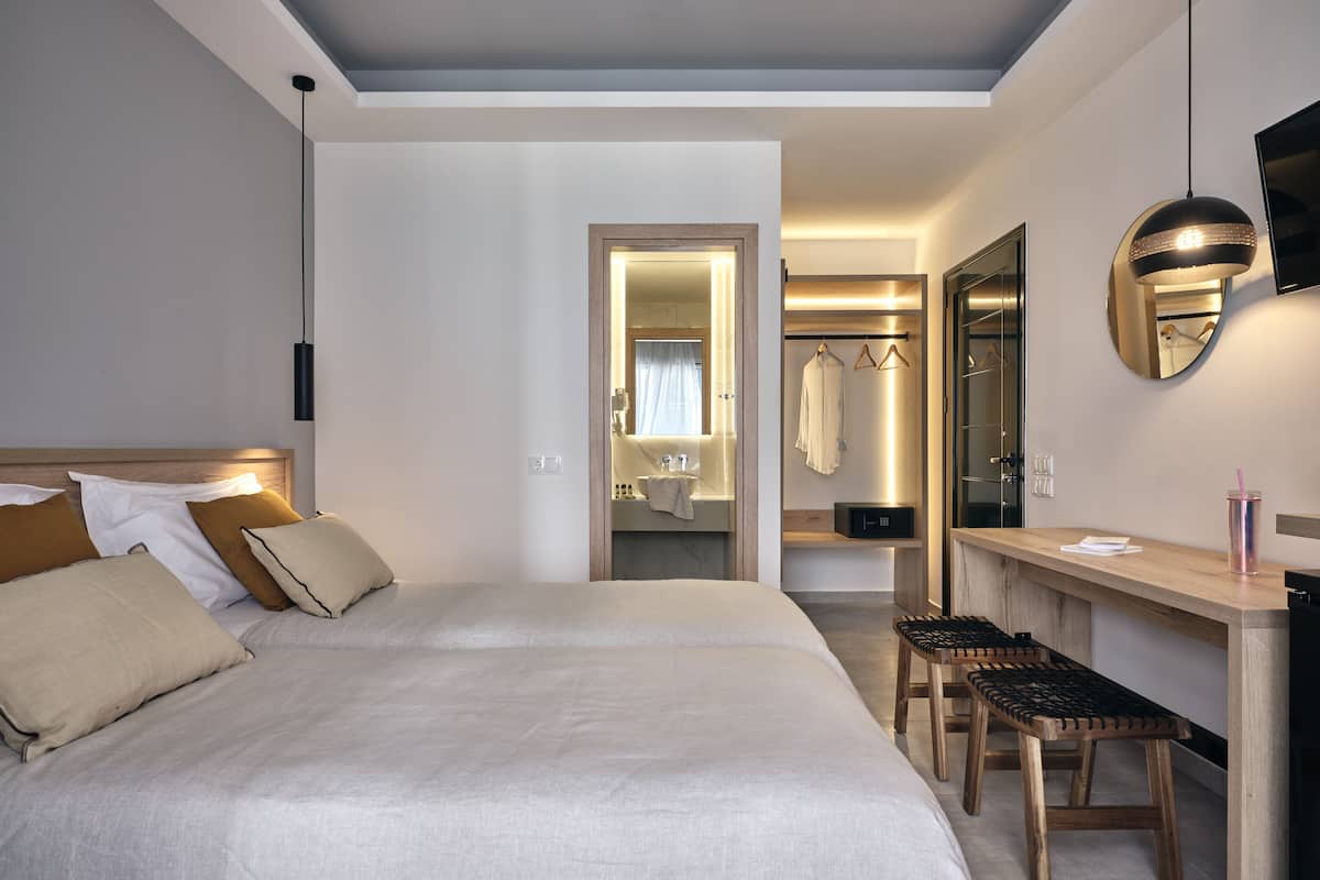 Una habitación de hotel con dos camas, un escritorio, una silla, un espejo y un televisor.