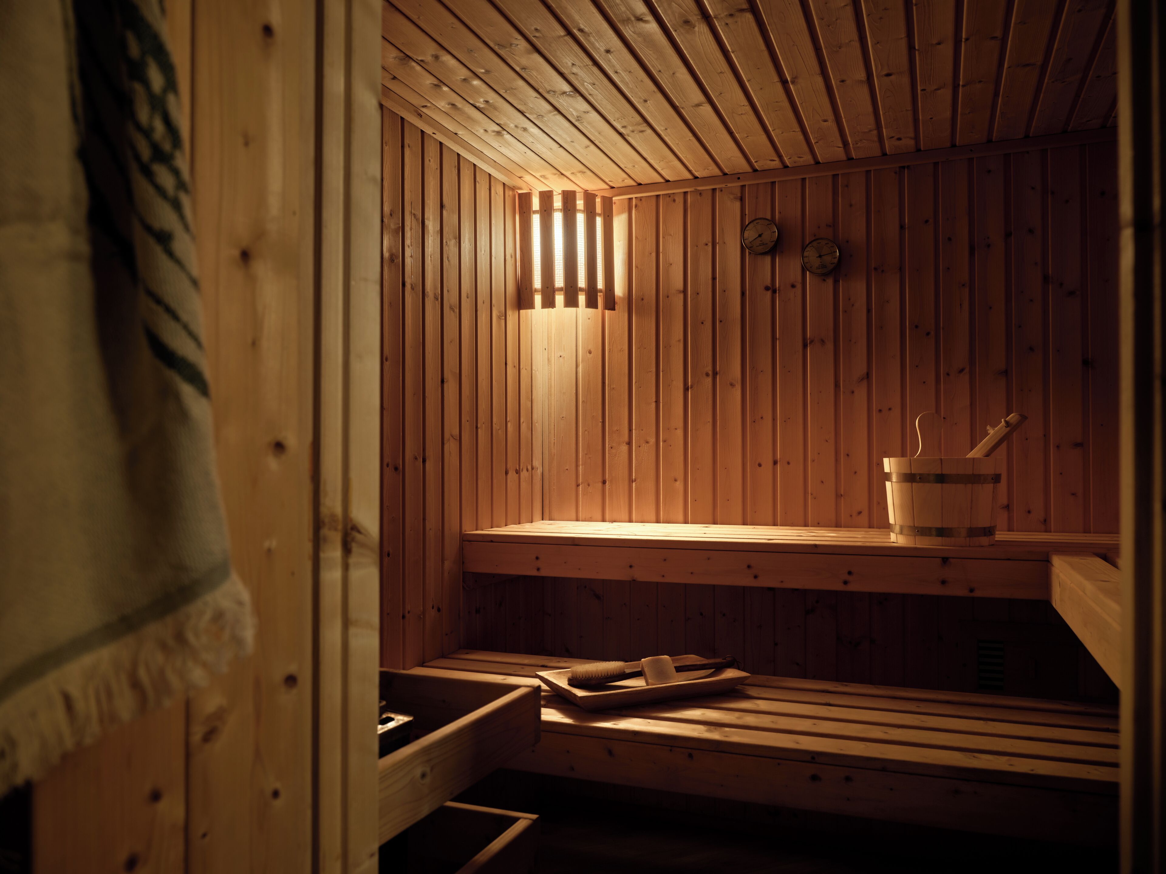 A sauna with wooden walls and benches, a bucket with a brush, and a towel hanging on the wall.