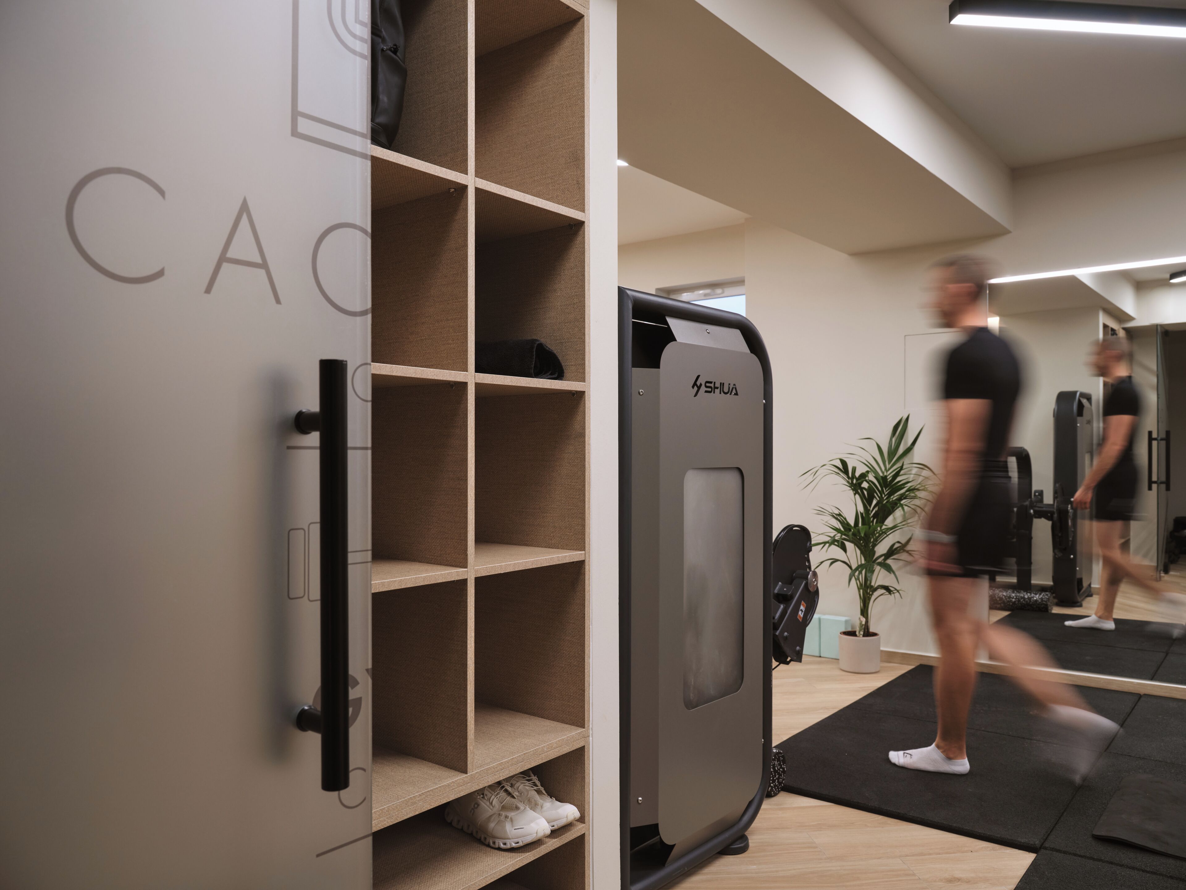 Ein Fitnessraum mit Trainingsgeräten, einer Spiegelwand und einem Schuhregal.