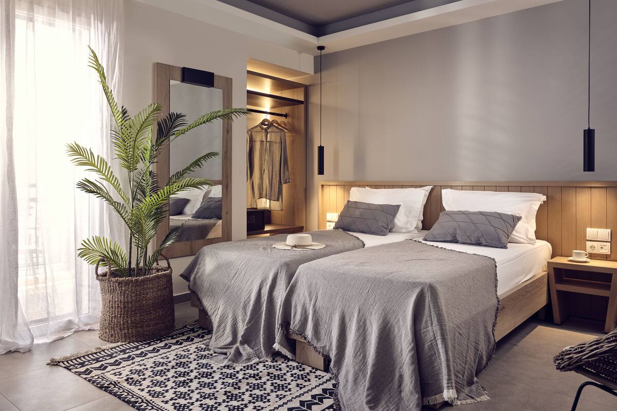 Un dormitorio moderno con dos camas, un espejo grande, una lámpara colgante y una planta en maceta.