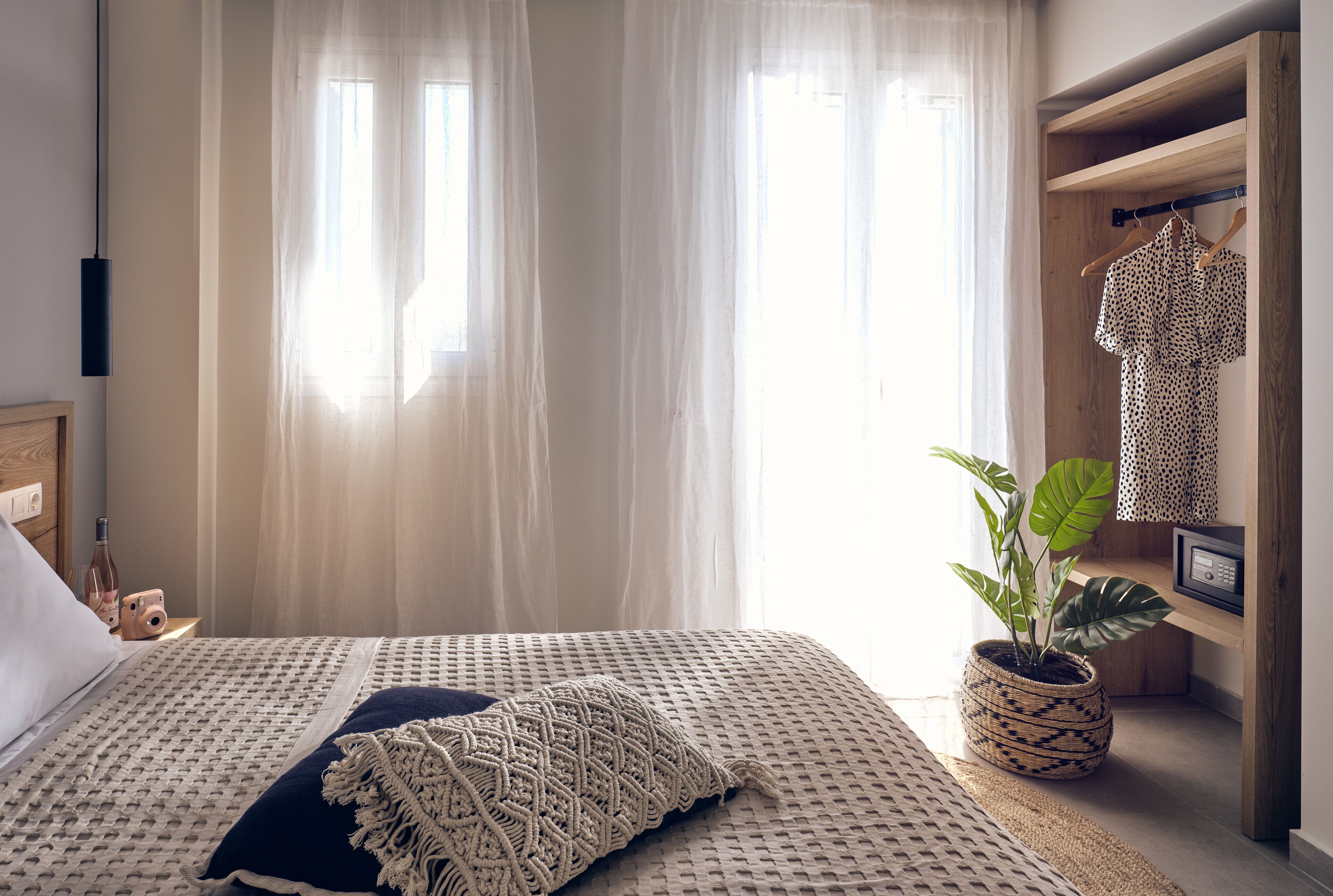 A neatly made bed with a patterned bedspread, a potted plant, and a wooden shelf with a garment.