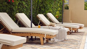 A row of sun loungers with umbrellas, a patterned floor, and a green hedge in the background. - Cactus Hotel (Zakynthos)