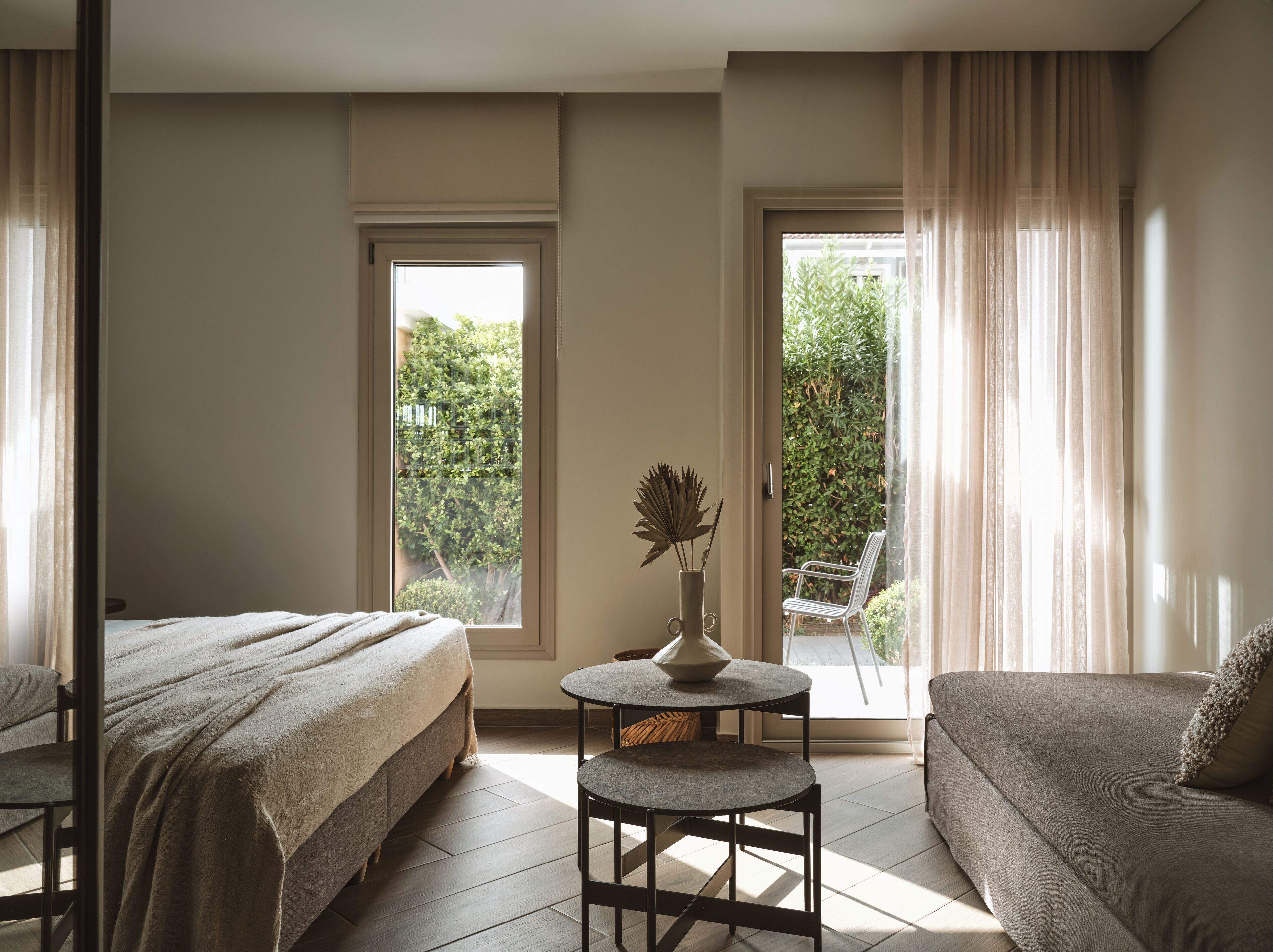 A hotel room with two beds, a small round table, and a view of greenery outside.