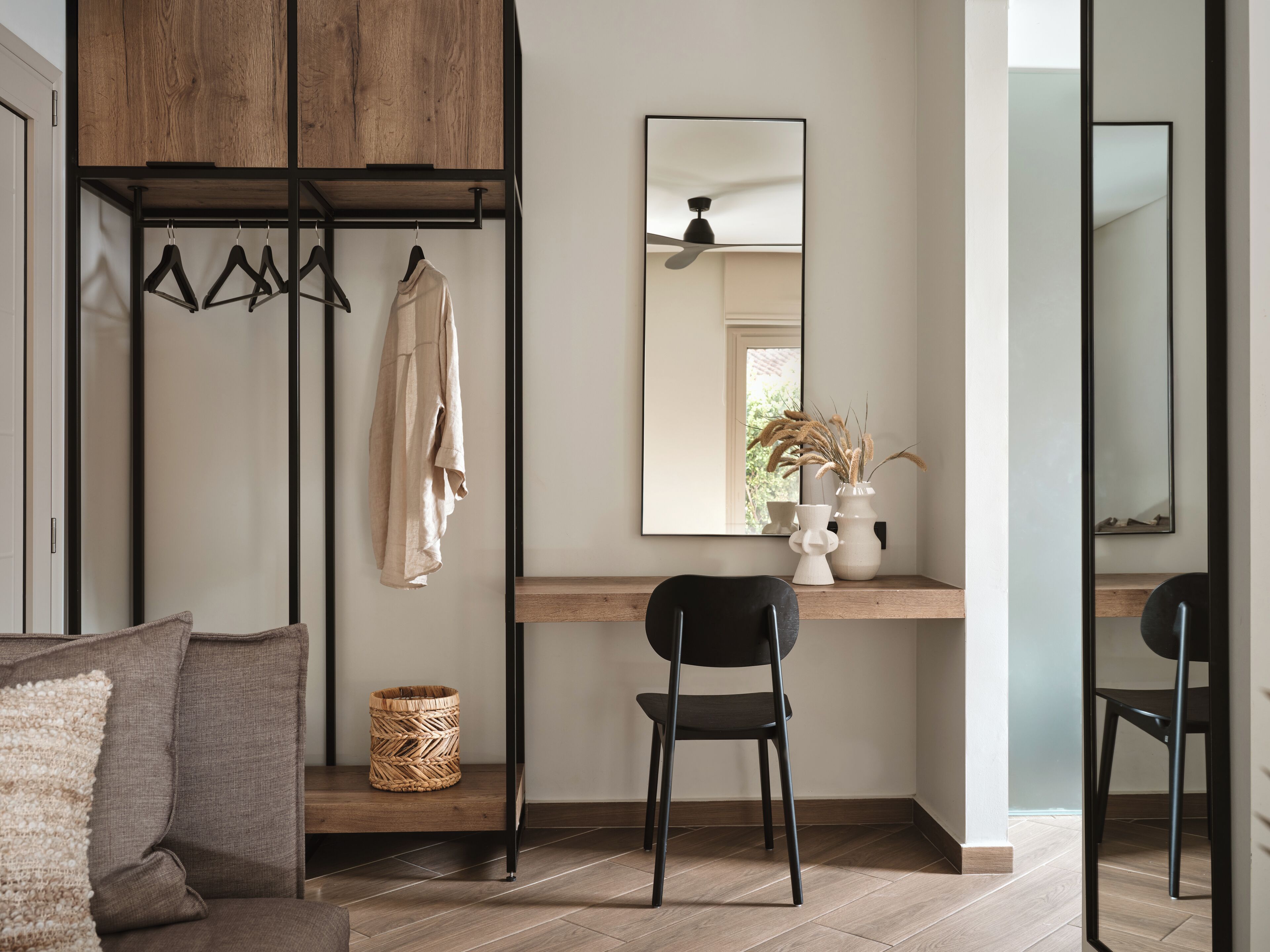 A modern room with a wooden wardrobe, a mirror, a desk with a chair, and a woven basket.