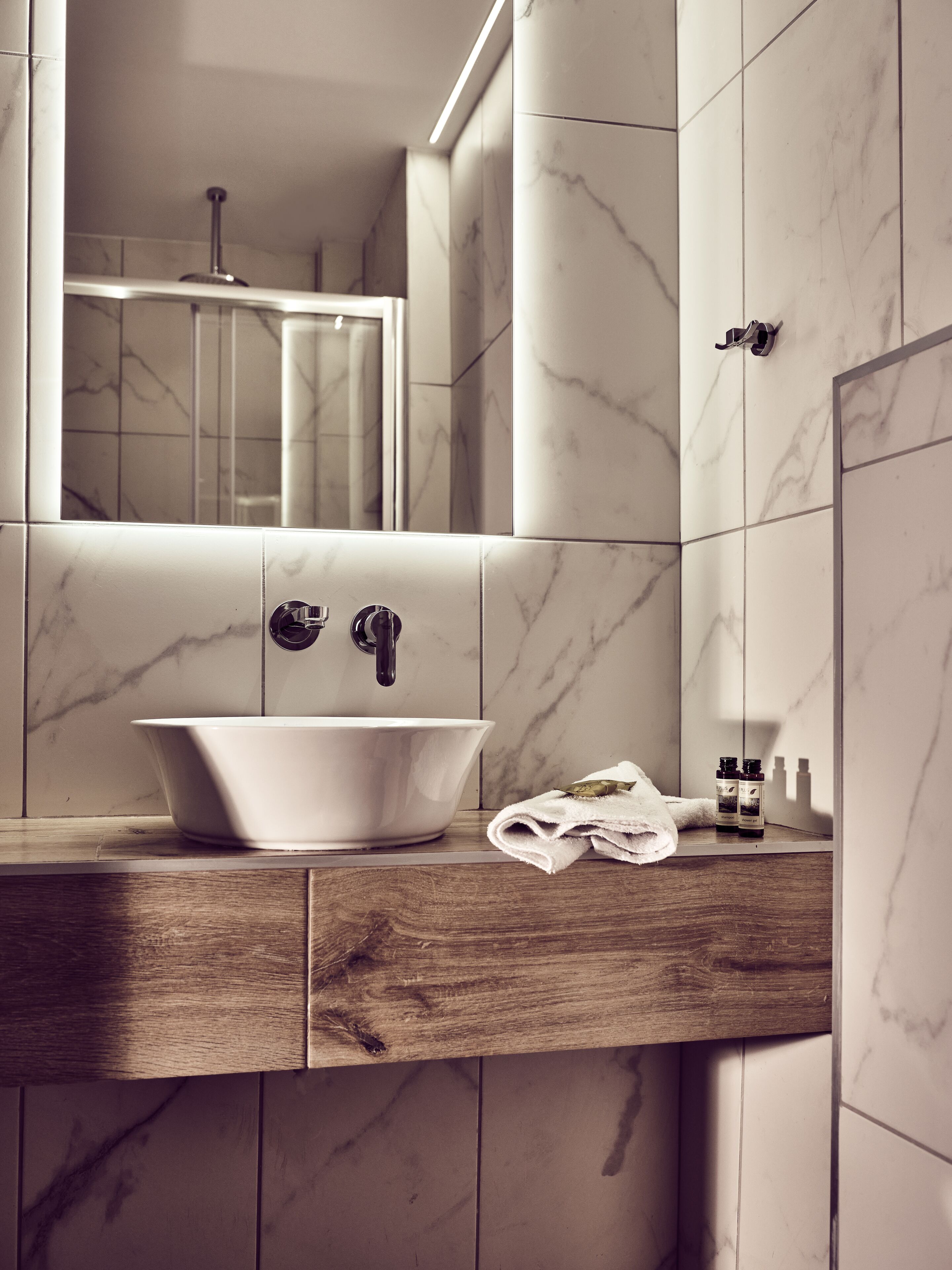 Un baño con lavamanos de mármol, encimera de madera y un espejo sobre el lavamanos.