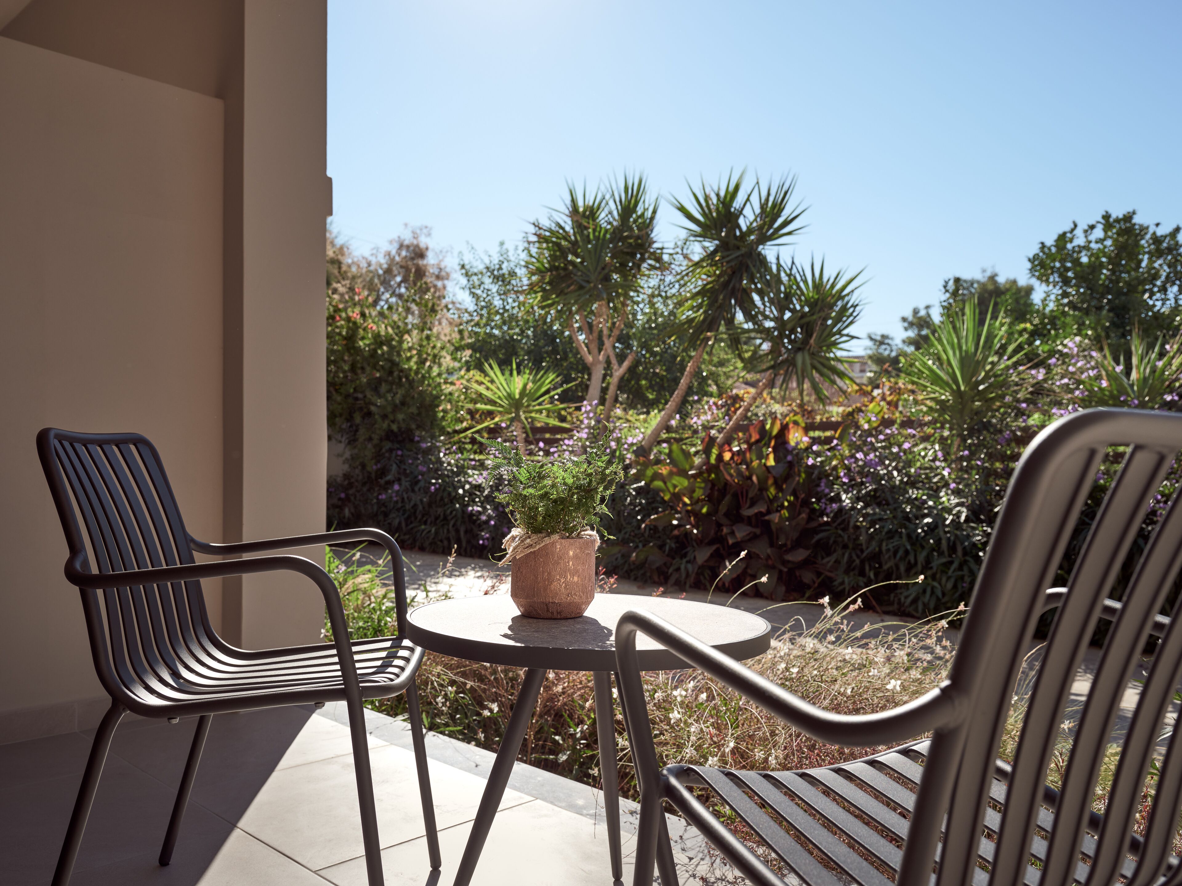 Une terrasse avec deux chaises en métal et une petite table ronde, entourée de différentes plantes et arbres.