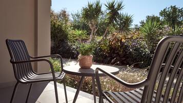 A patio with two metal chairs and a small round table, surrounded by various plants and trees.