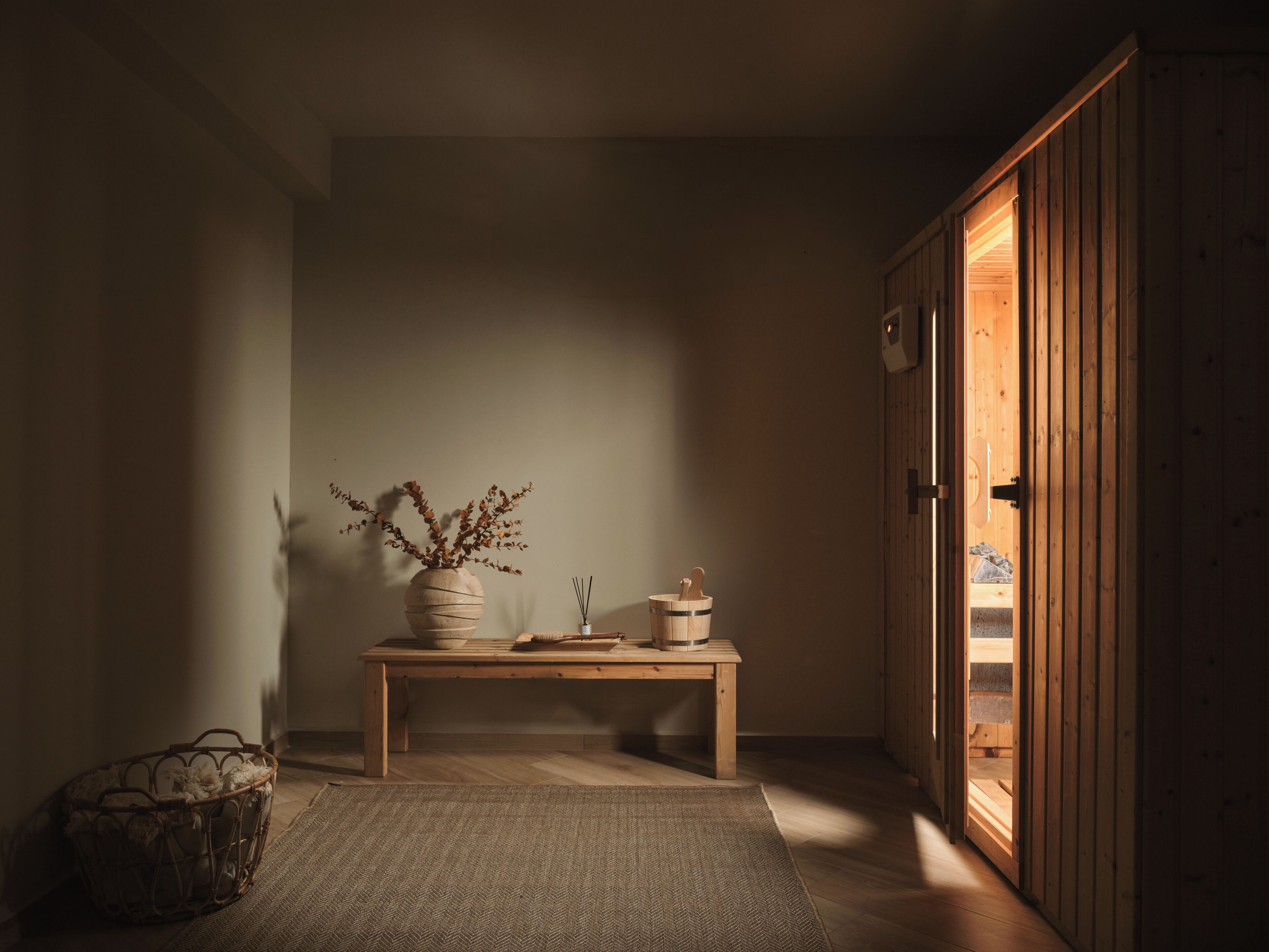 Una habitación con piso de madera, un tapiz tejido, una mesa de madera con un jarrón y un pequeño recipiente, y un armario de madera.