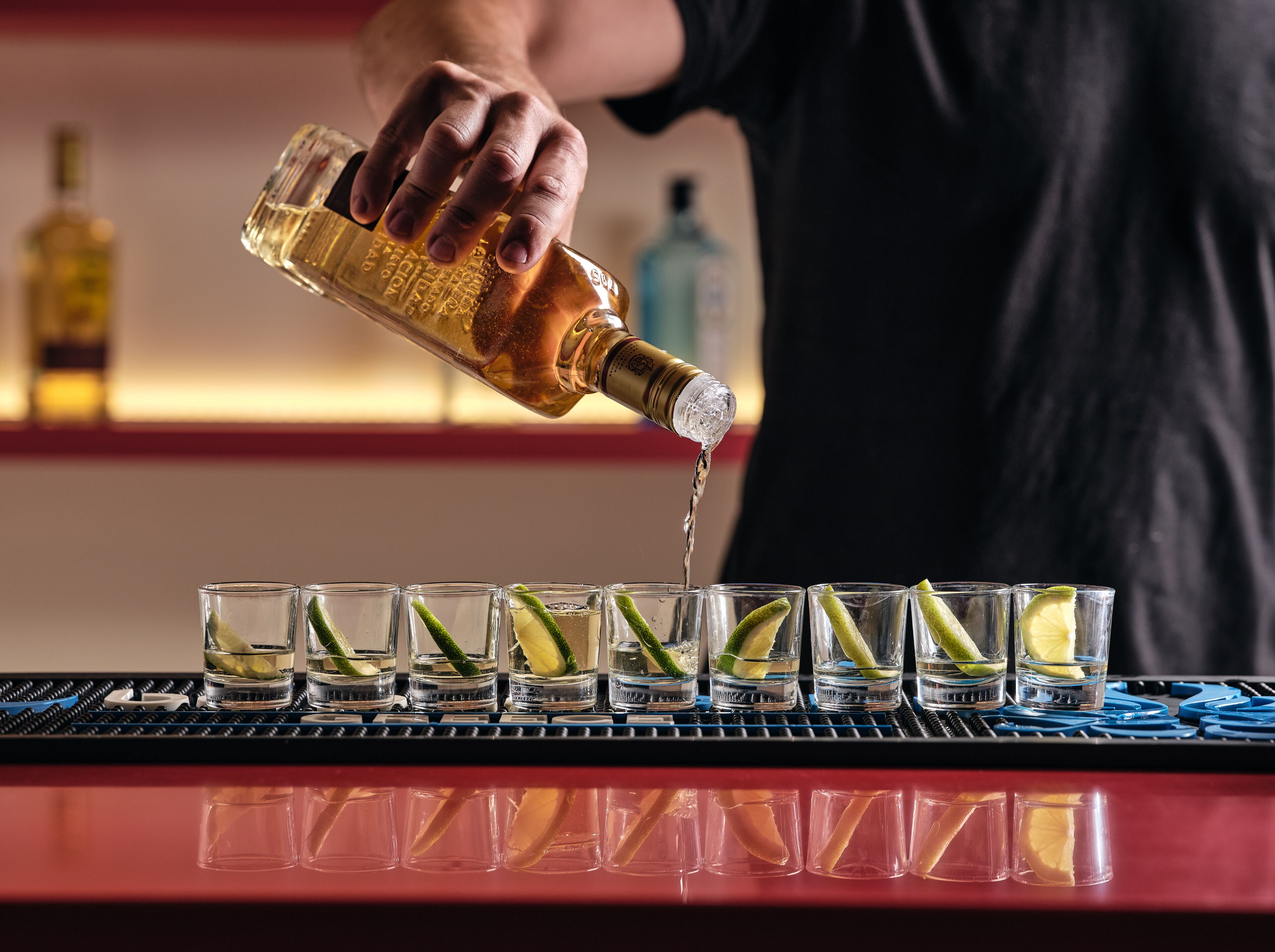 A bartender pouring a clear liquid into glasses with lime wedges.