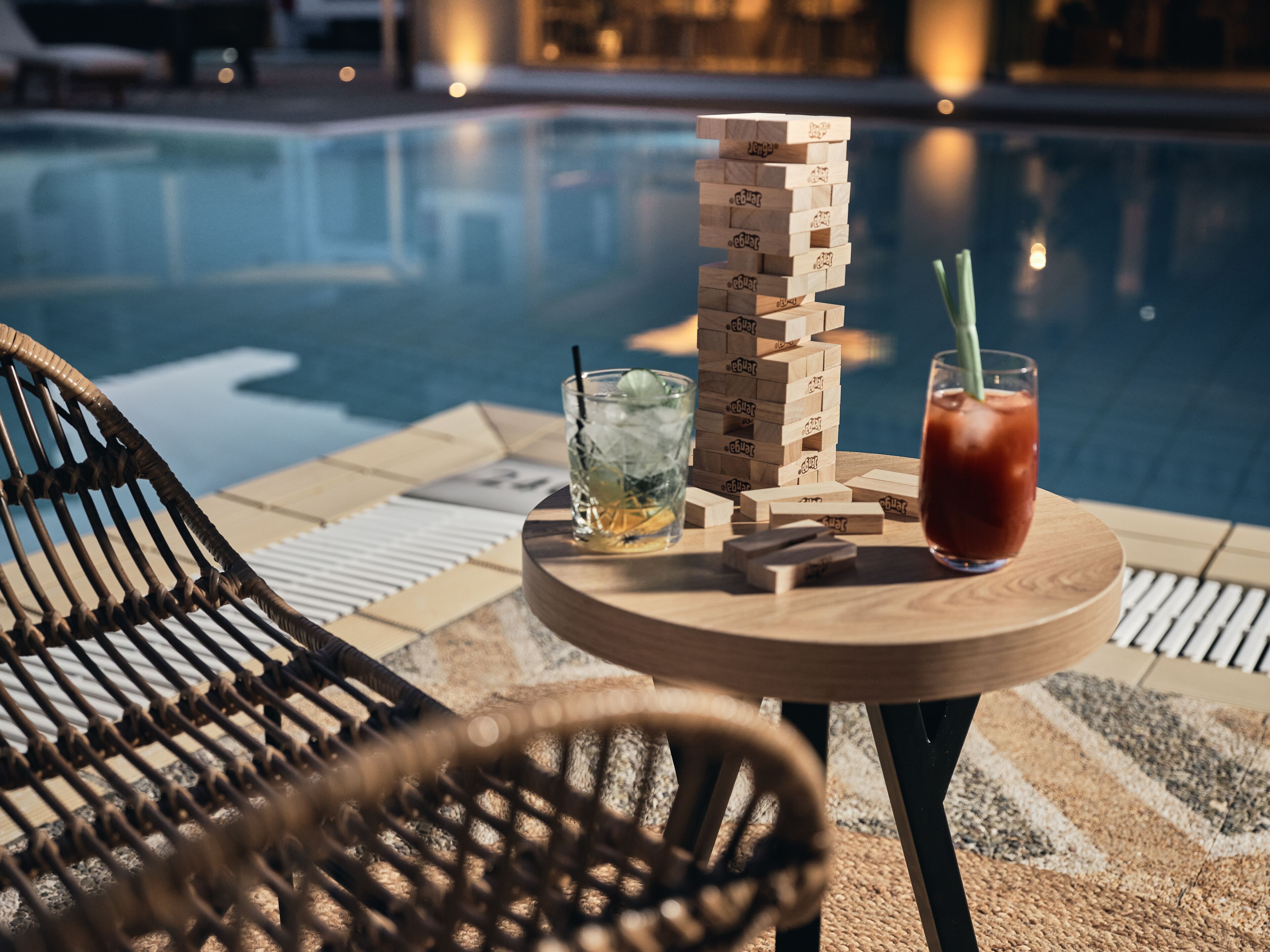 A poolside setting with a wooden block game, a glass with a straw, and a chair.