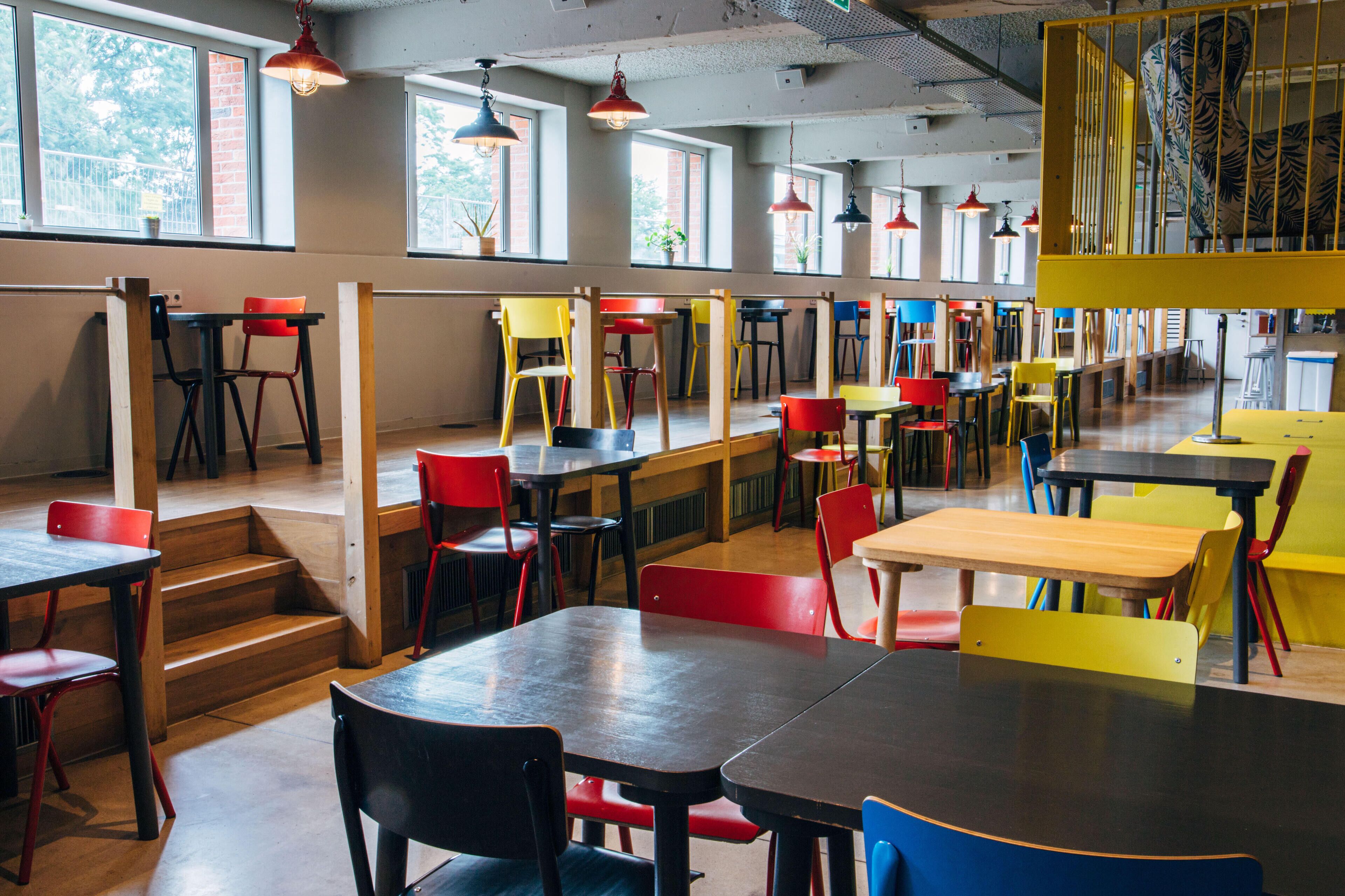 A spacious dining area with multiple tables and chairs, large windows, and hanging pendant lights.