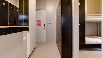 A corridor with lockers, a door with a sign, and a bunk bed area.
