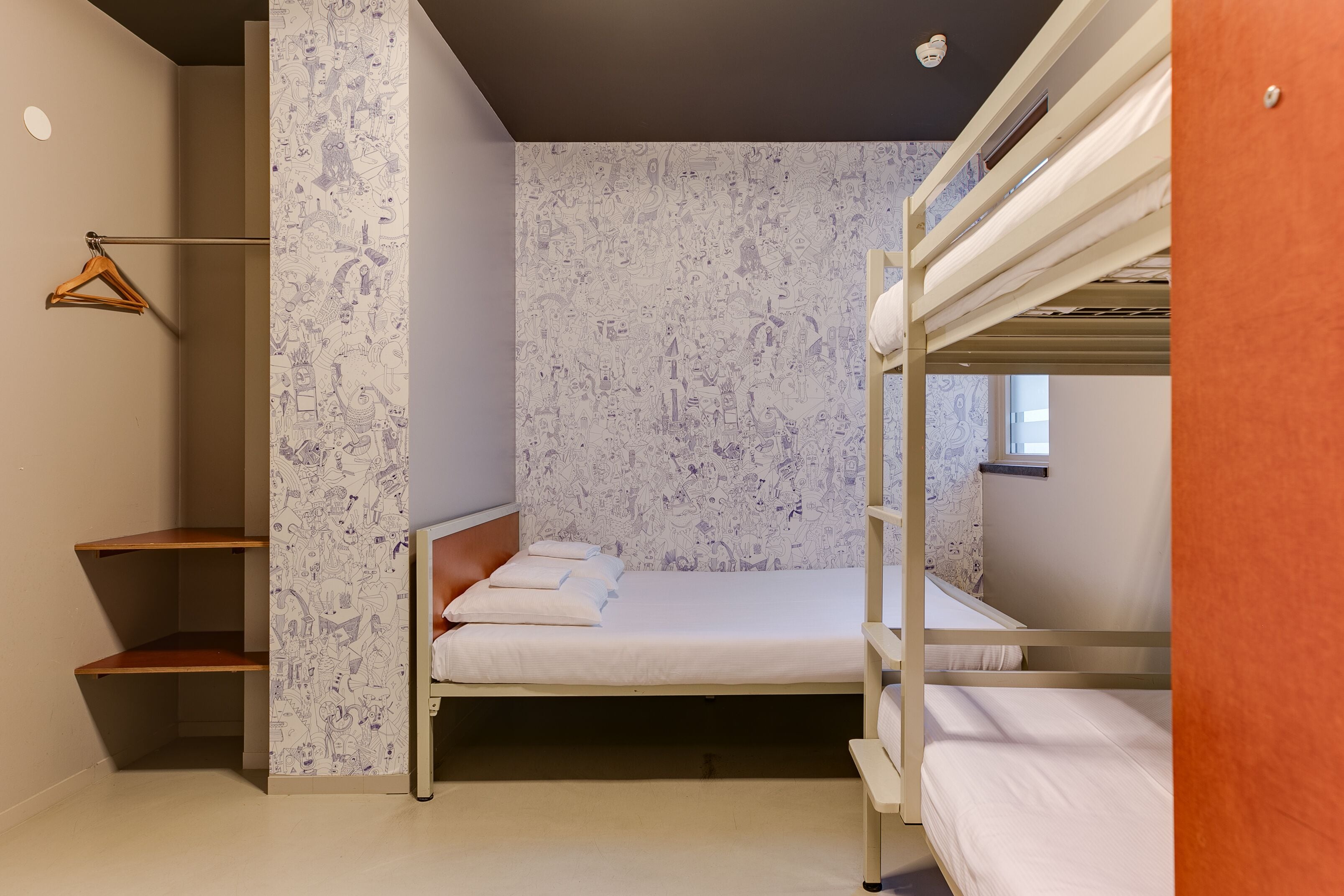 Een slaapkamer met stapelbed, behang met patroon, een houten plank en een kledingroede.