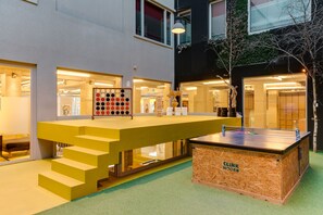 A modern indoor space with a yellow staircase leading to a reception area, a ping pong table, and a wooden box labeled 'CLINK NOORD'. - ClinkNOORD - Hostel (Amsterdam)