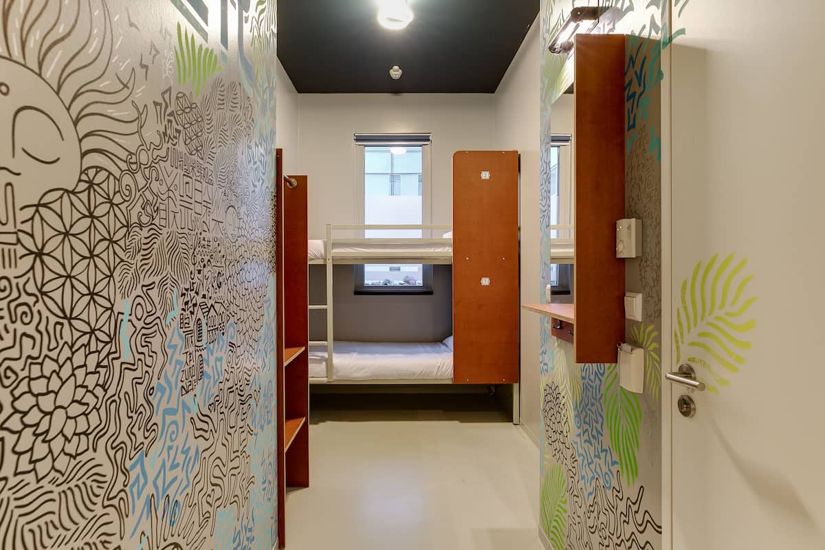 A room with a bunk bed, a window with blinds, a door with a handle, and a wall with a patterned design.