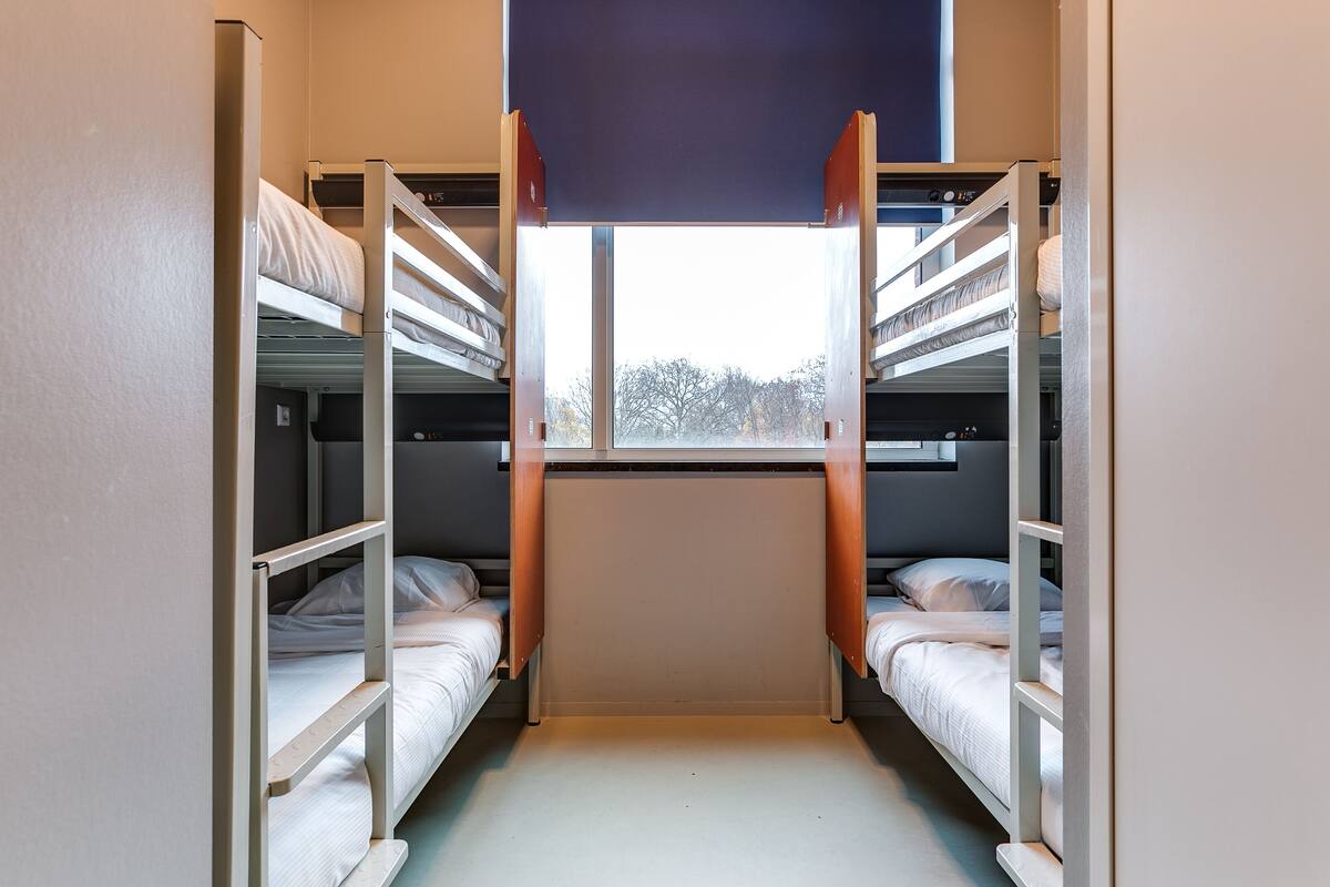 A dormitory room with bunk beds, a window, and a door.