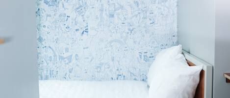 Un dormitorio con cama, ropa de cama blanca y una pared con un diseño azul de garabatos.