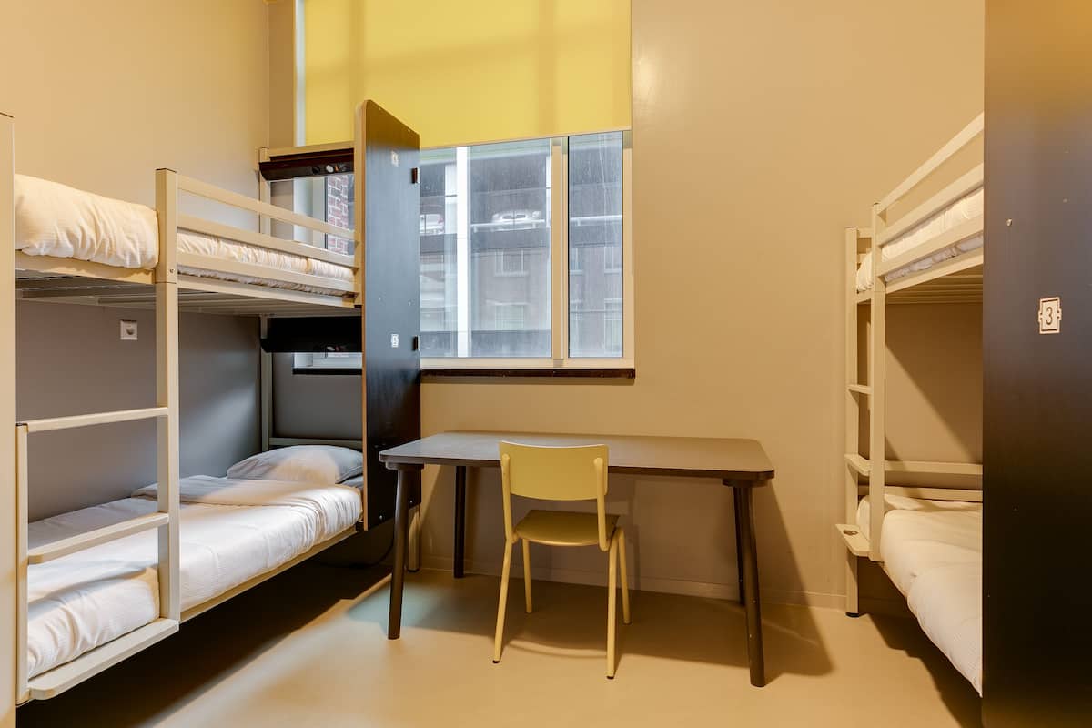 A dormitory room with bunk beds, a desk, and a chair.