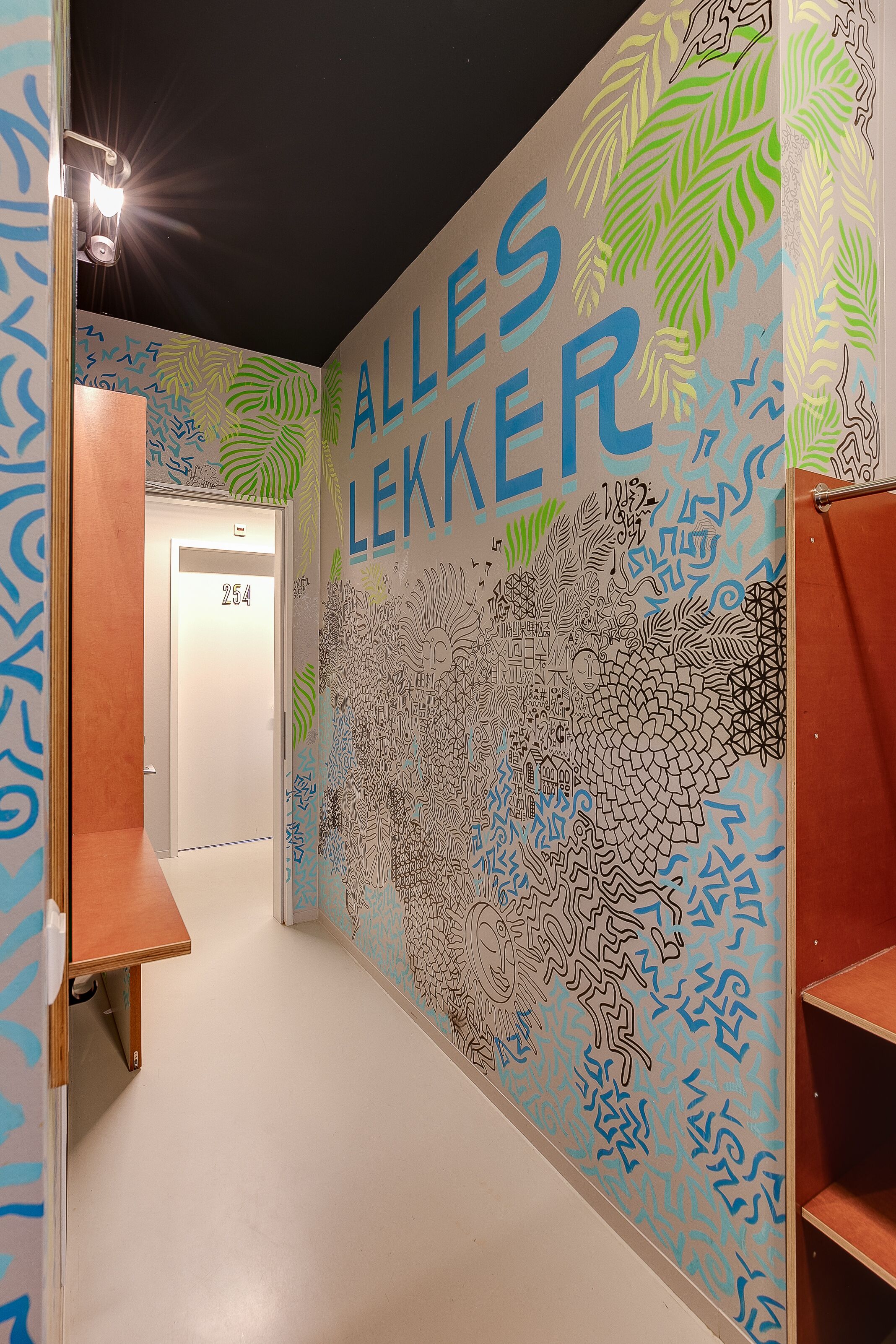 Un pasillo con un mural que presenta patrones abstractos y el texto "ALLES LEKKER".