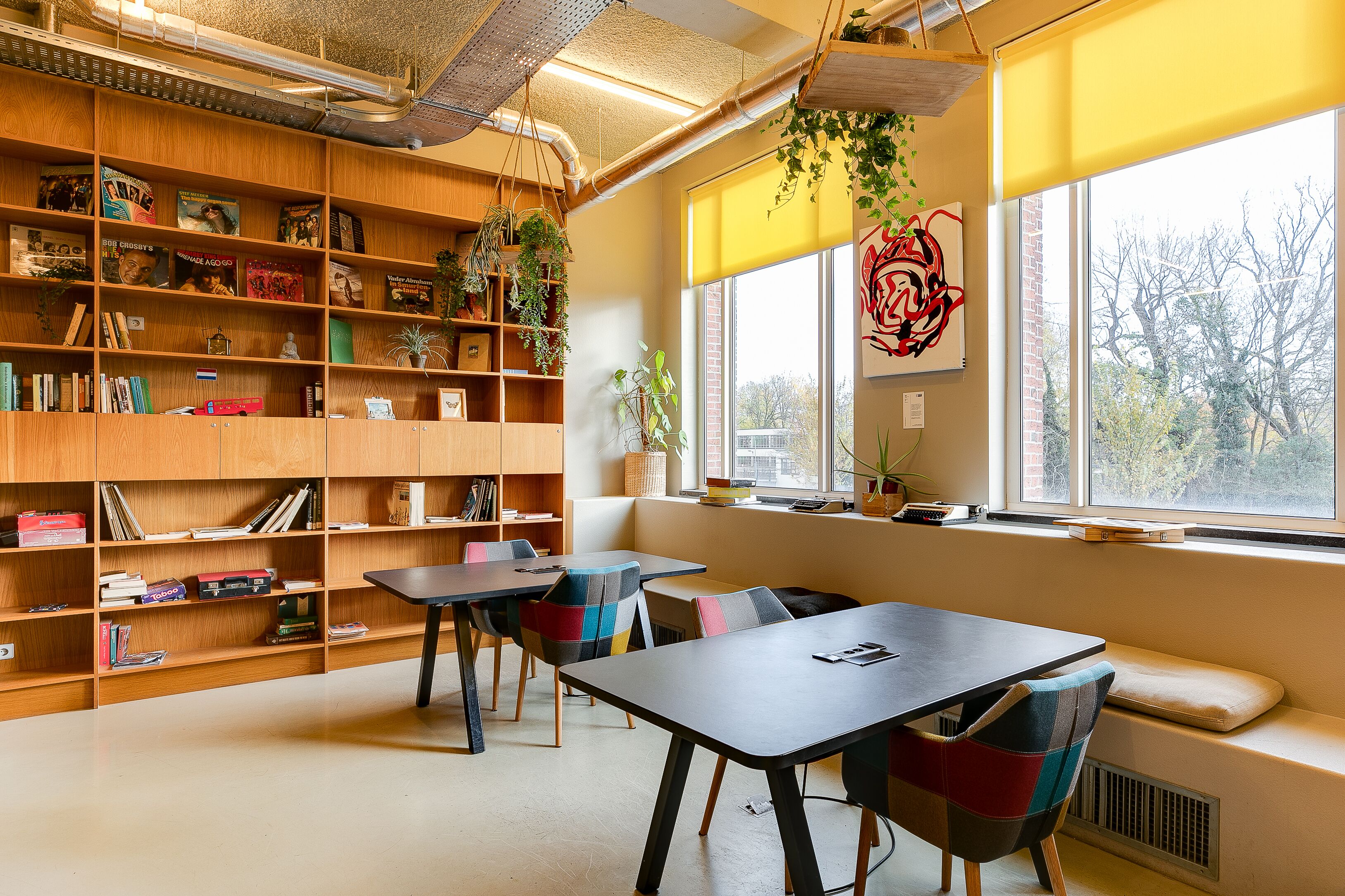 Una biblioteca con estanterías de madera, una mesa, sillas y un ventanal con vistas.