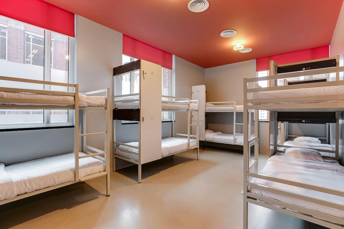 A dormitory room with bunk beds, a window, and a door.