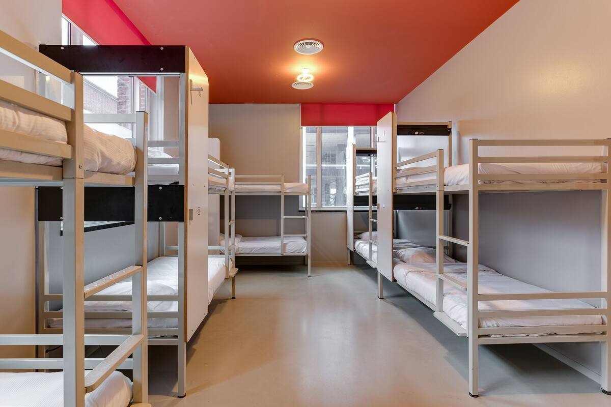 A dormitory room with bunk beds, a window, and a red ceiling.