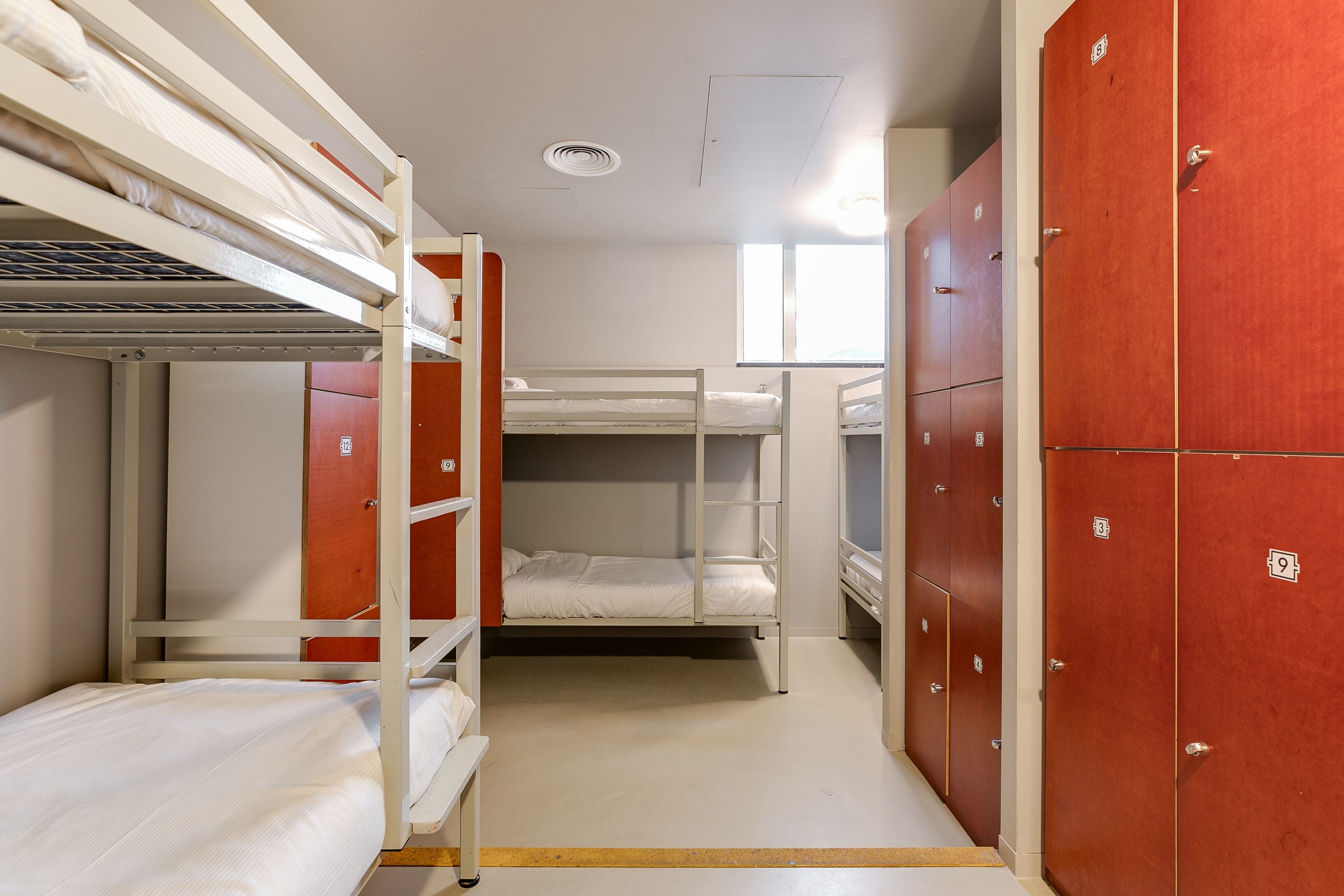 A dormitory room with bunk beds, wooden lockers, and a window providing natural light.